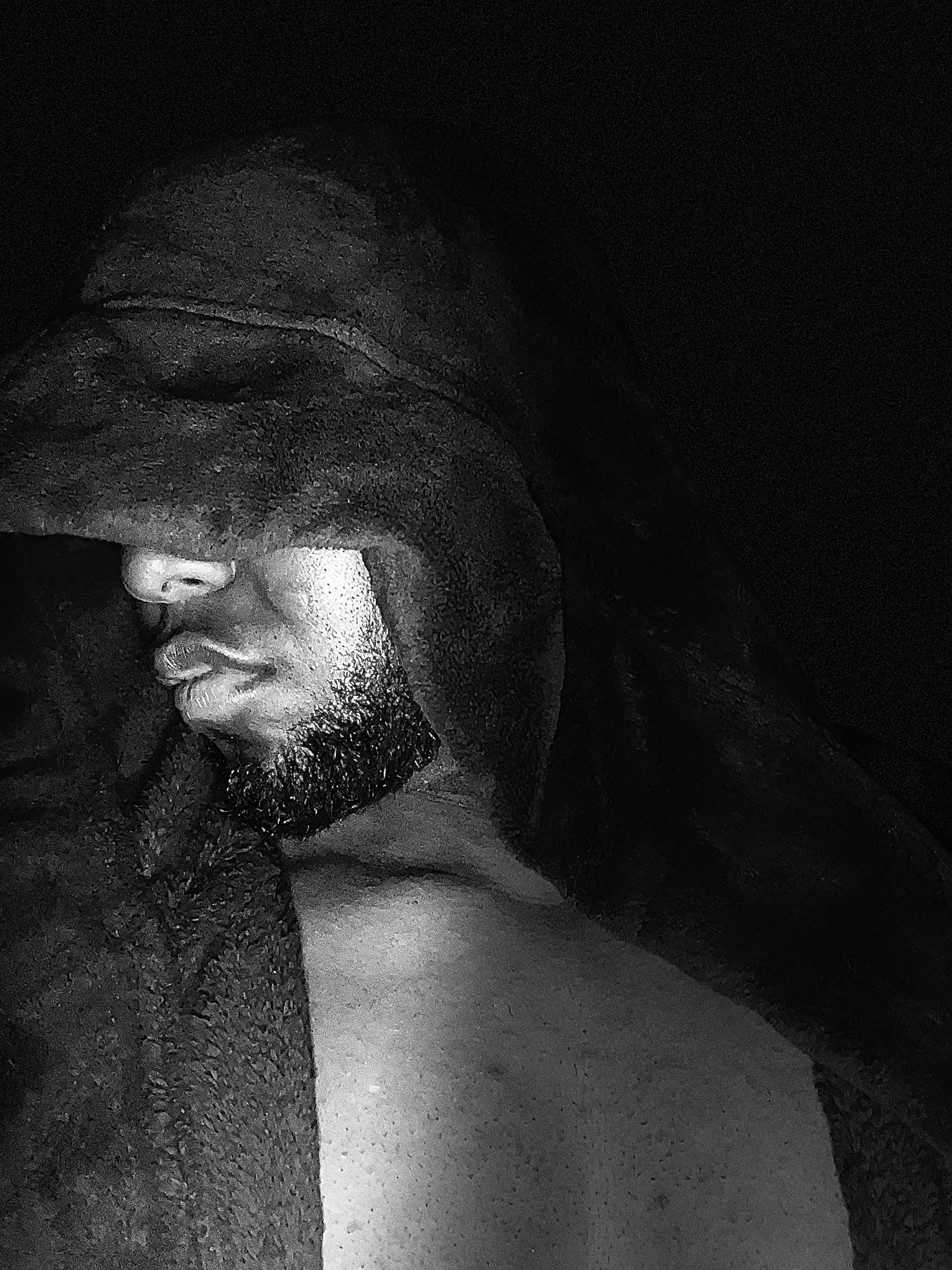 Close-up of a stone sculpture of a person's face, with a beard and closed eyes, carved into dark stone, partially obscured by shadow.