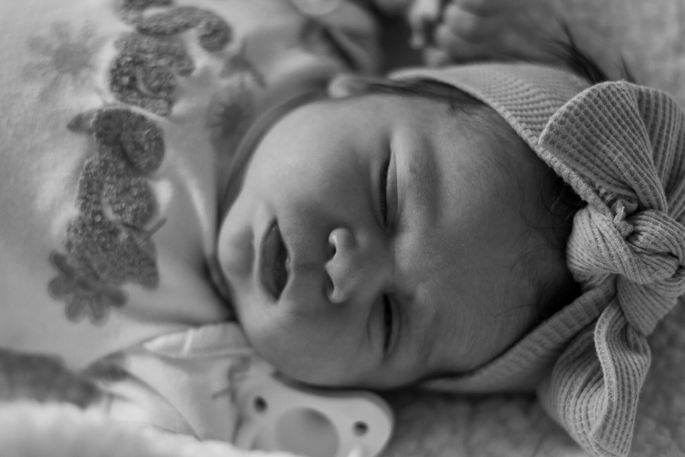 Close-up of a newborn baby sleeping, wrapped in a knitted blanket, with a decorative lace border visible.