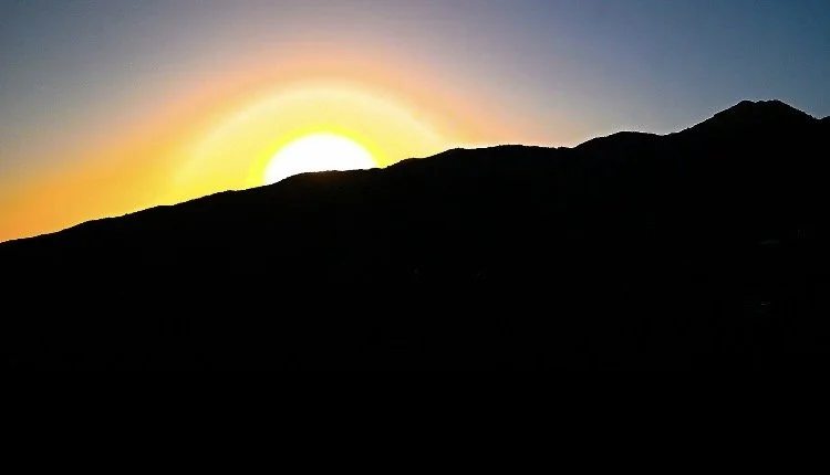 Sunset behind mountain silhouette with colorful sky.