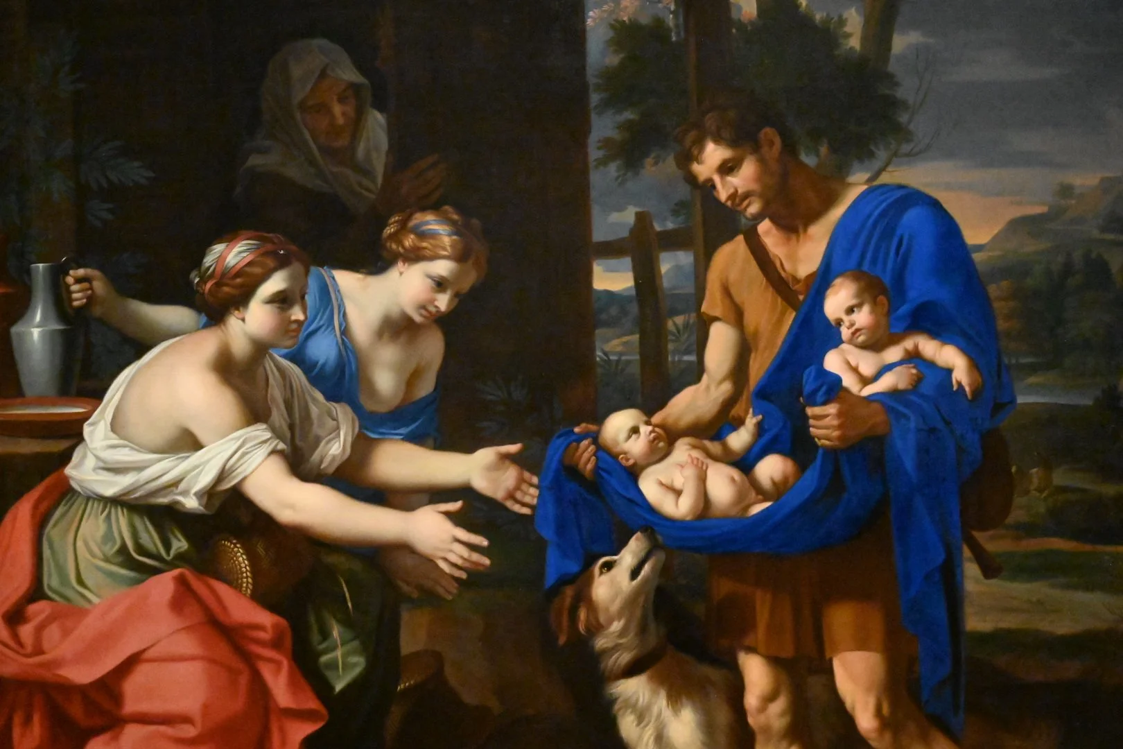 A religious painting depicting the nativity scene with Mary and Joseph adoring baby Jesus, who is lying in a manger, with a dog looking up at Jesus and a woman offering a gift in the background.