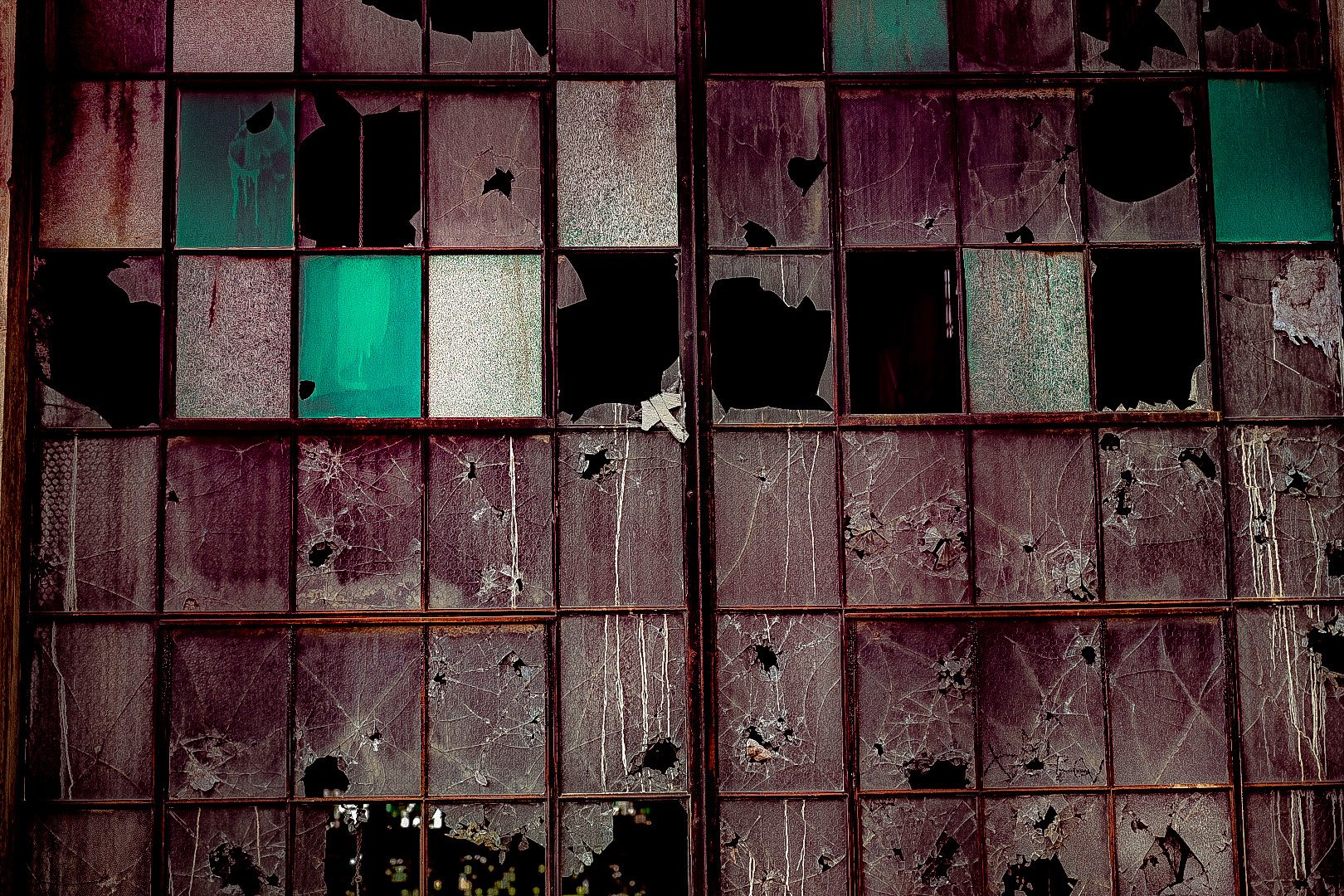 A large, rusty window with multiple panes of broken and cracked glass.