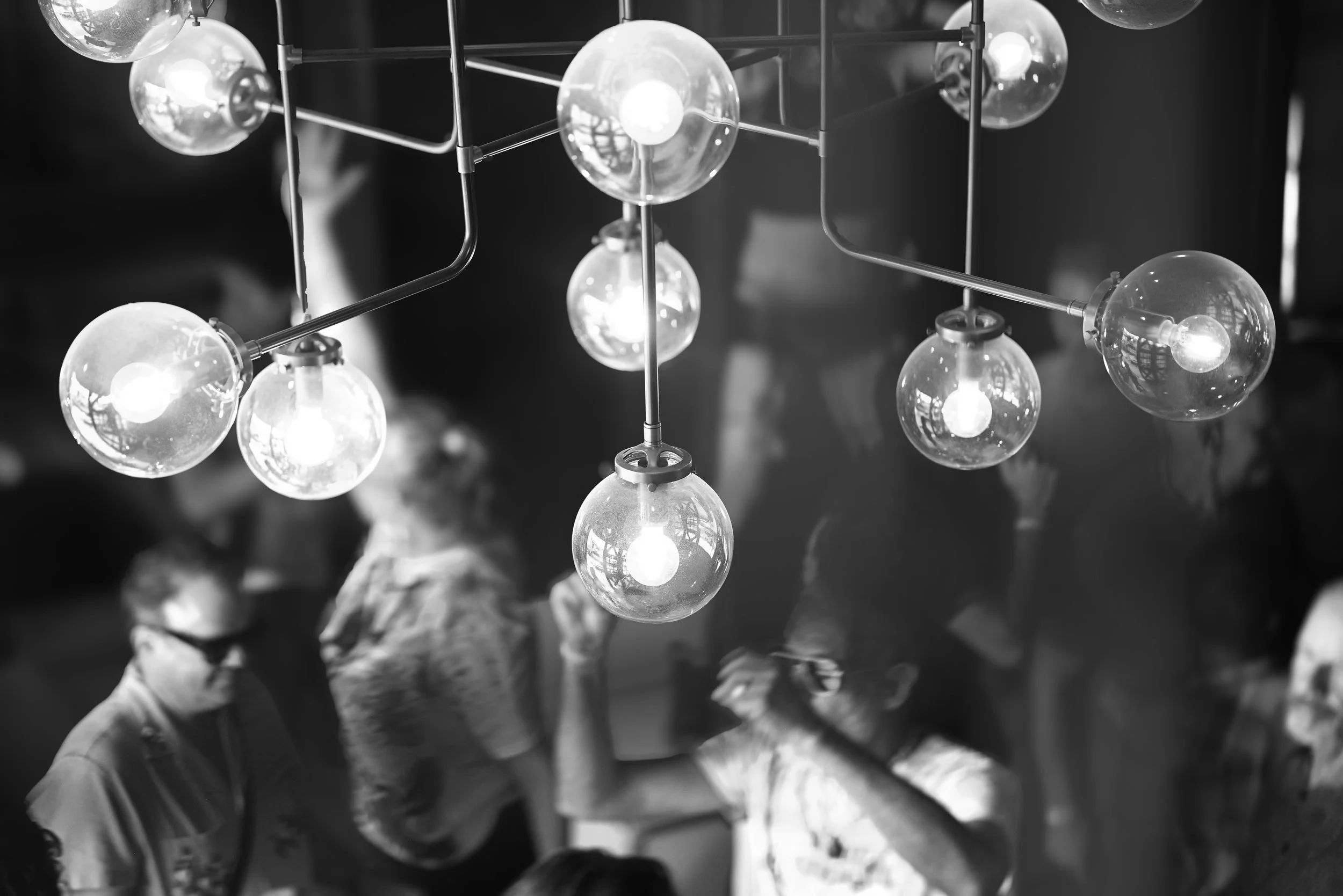Black and white photo of a modern chandelier with multiple glass globes, each containing a light bulb, suspended from a metal frame.
