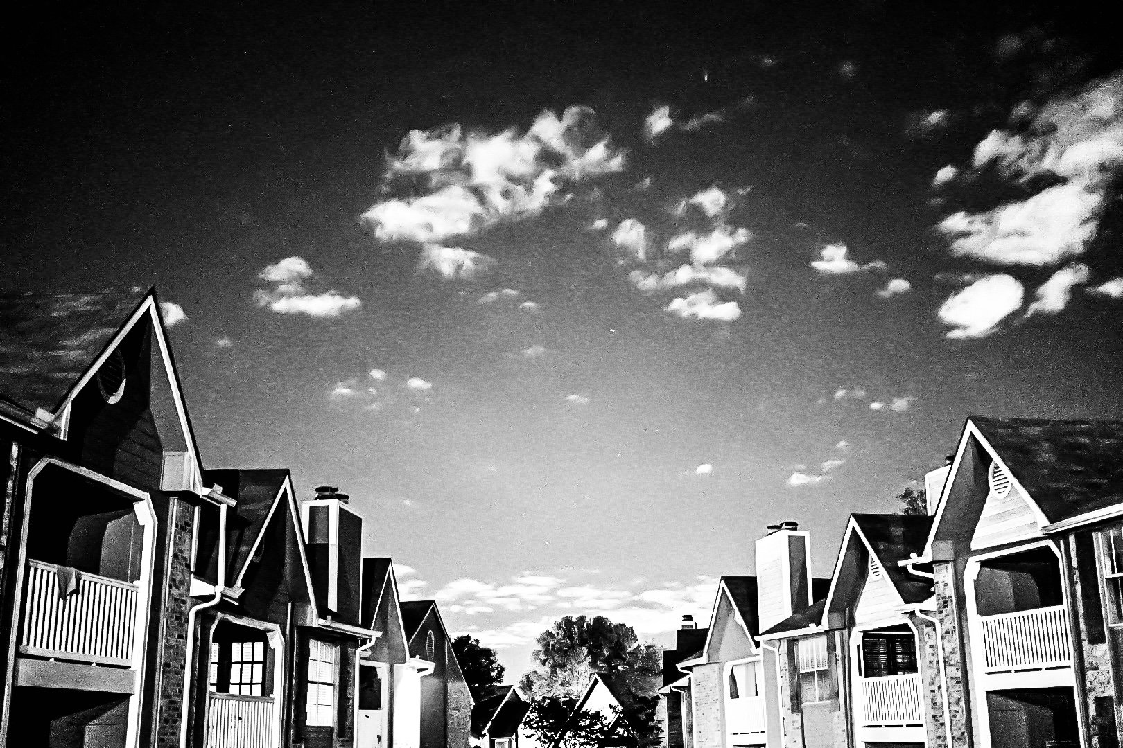 Black and white photo of a row of residential houses with pointed roofs and chimneys, under a night sky filled with scattered clouds and a visible star.