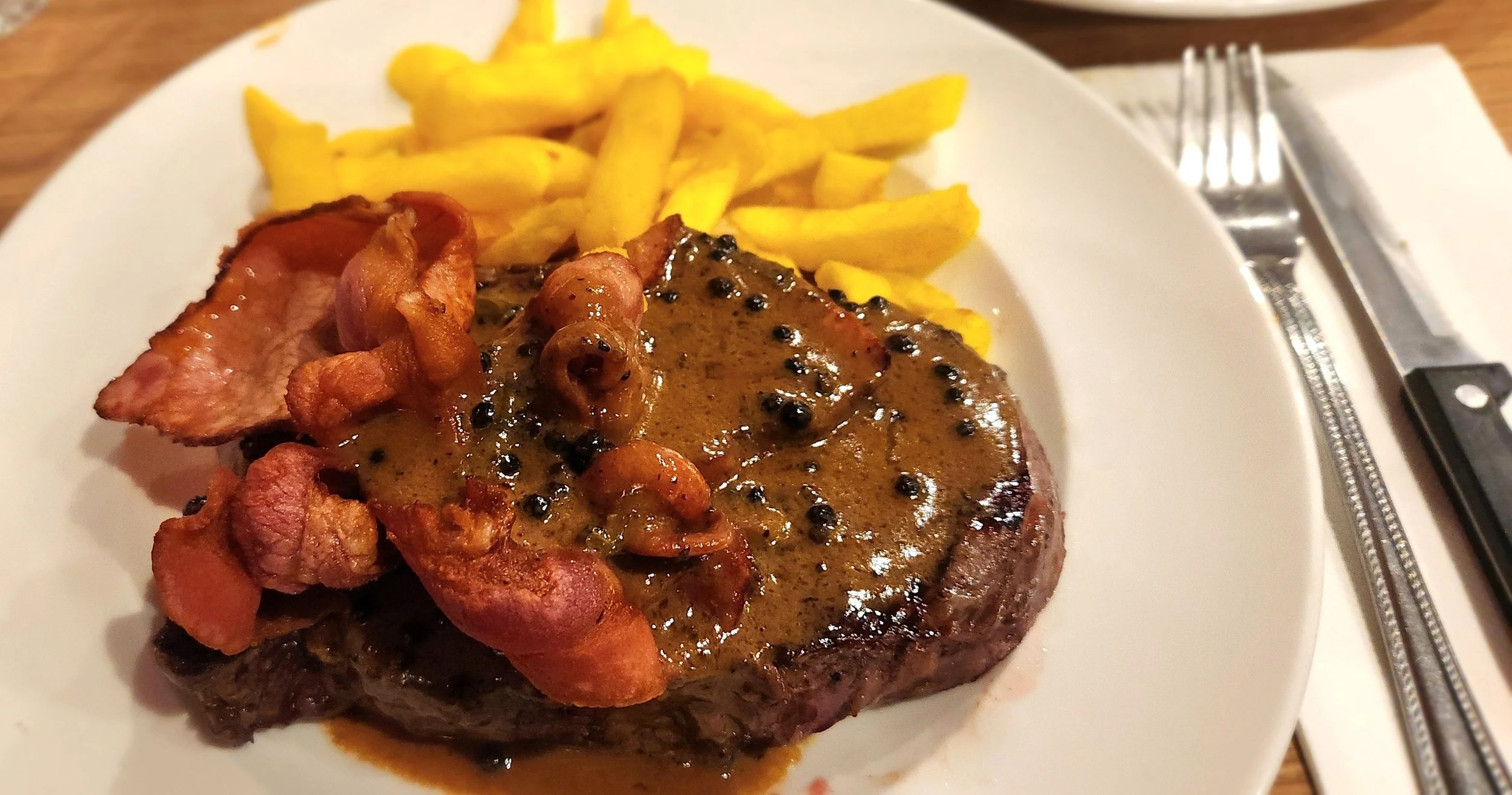 Steak with mushroom gravy, crispy bacon, and French fries on a white plate