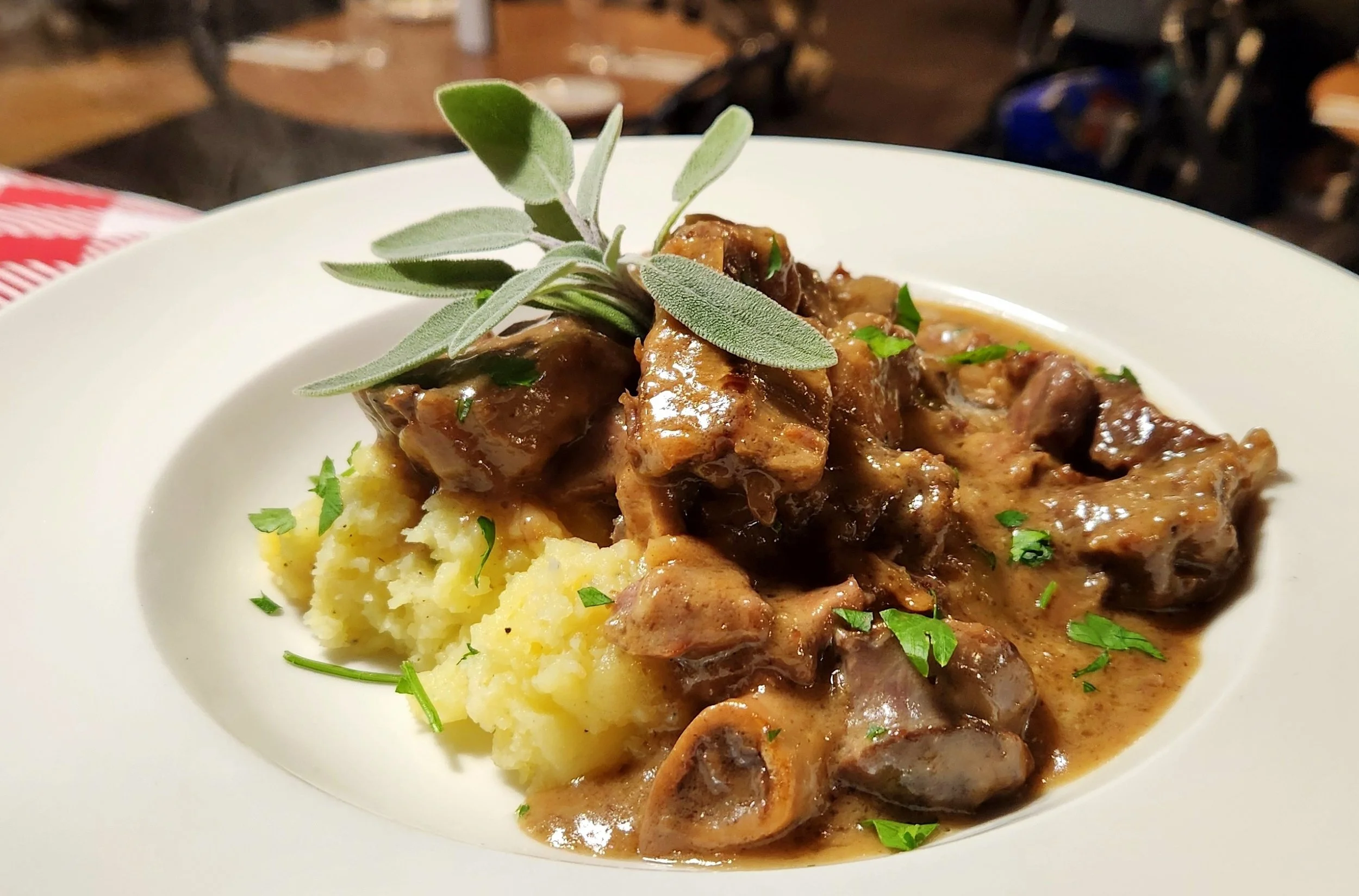 A plate with mashed potatoes topped with beef stew and garnished with fresh herbs.