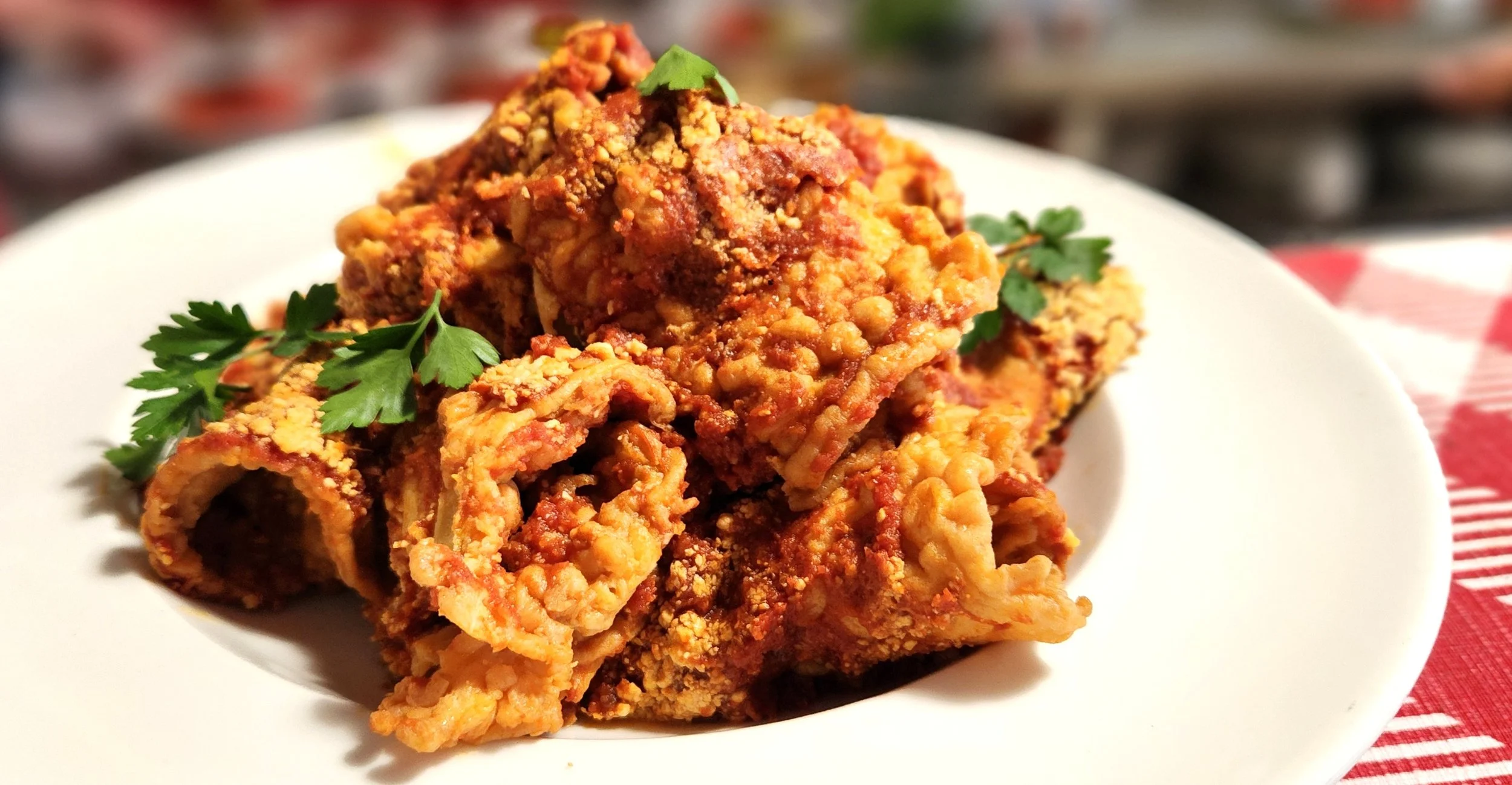 Close-up of fried chicken wings garnished with parsley on a white plate, with a blurred background and a red-and-white checkered tablecloth.