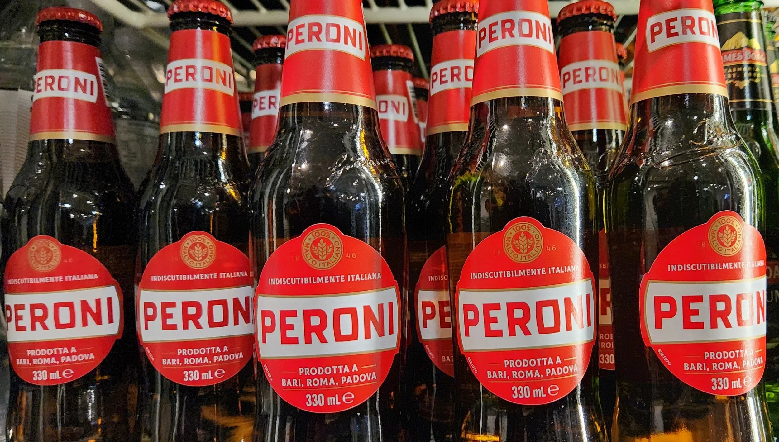Rows of Peroni beer bottles with red labels and white text, on a store shelf.
