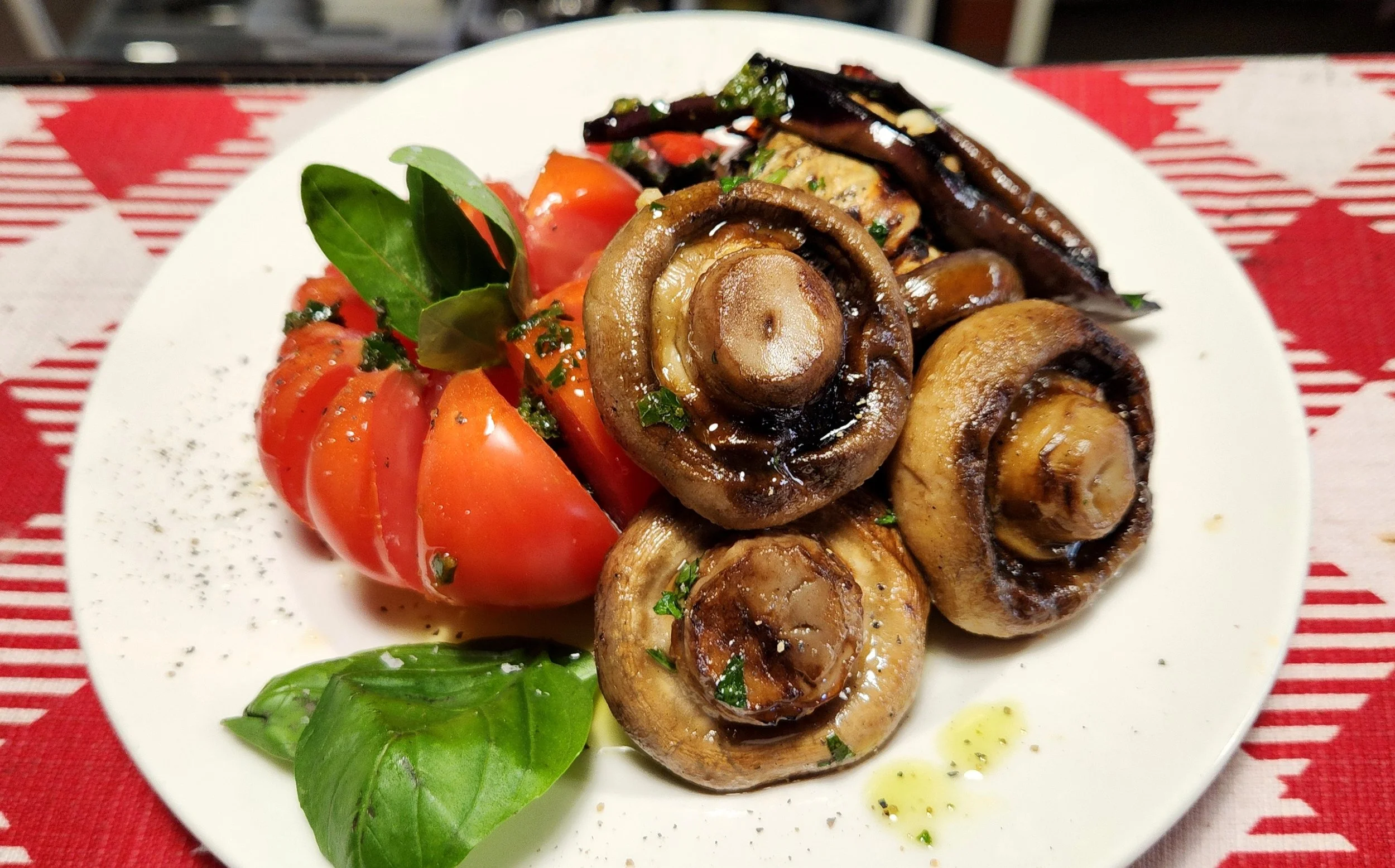 A plate of cooked mushrooms, heirloom tomatoes, and fresh basil leaves drizzled with olive oil and black pepper