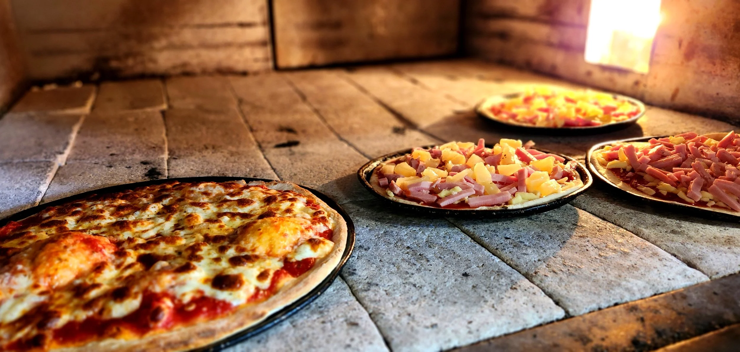 Multiple pizzas with different toppings baking in an oven with a brick interior.