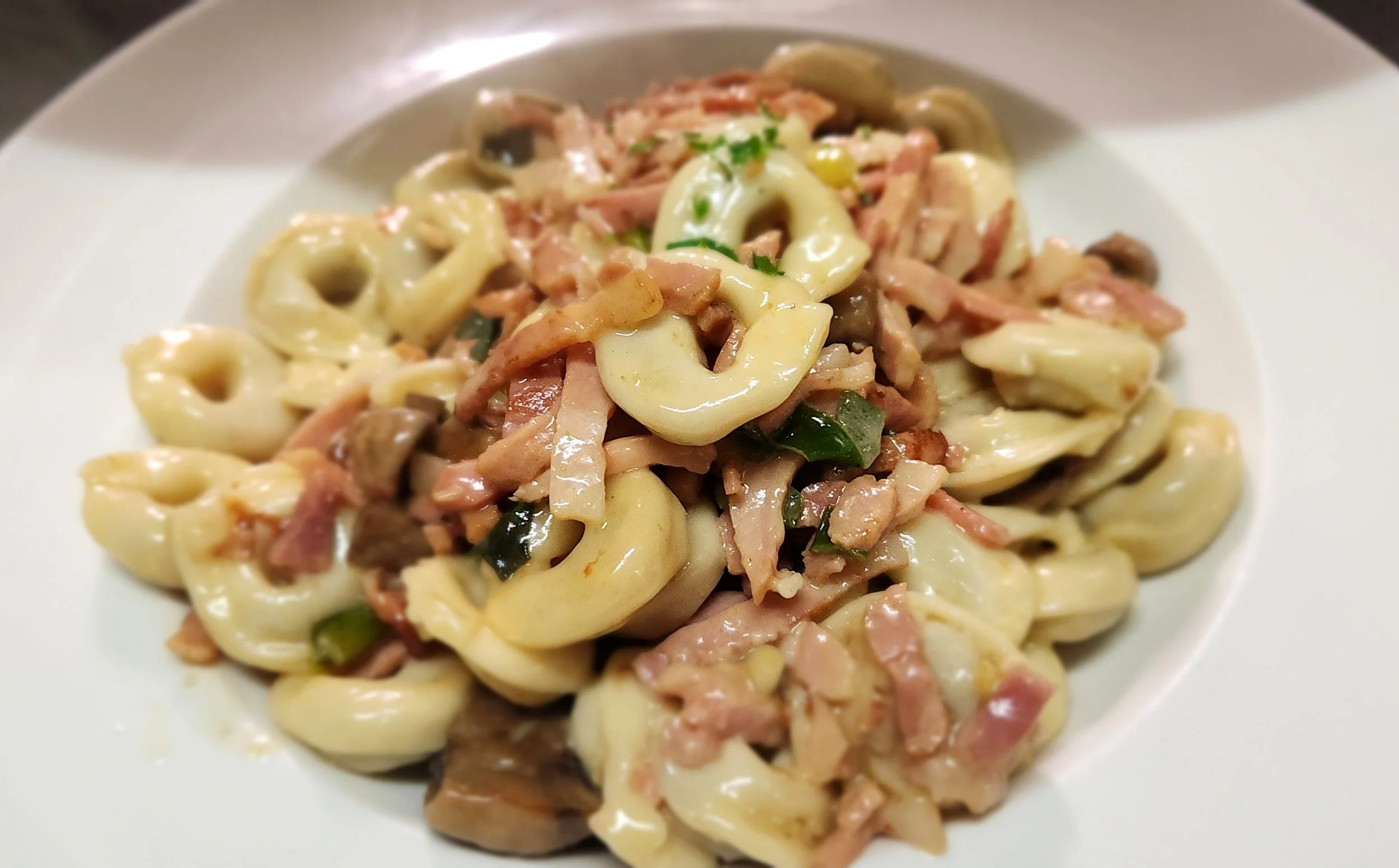 A white plate of creamy pasta with chunks of ham, mushrooms, and chopped green onions.