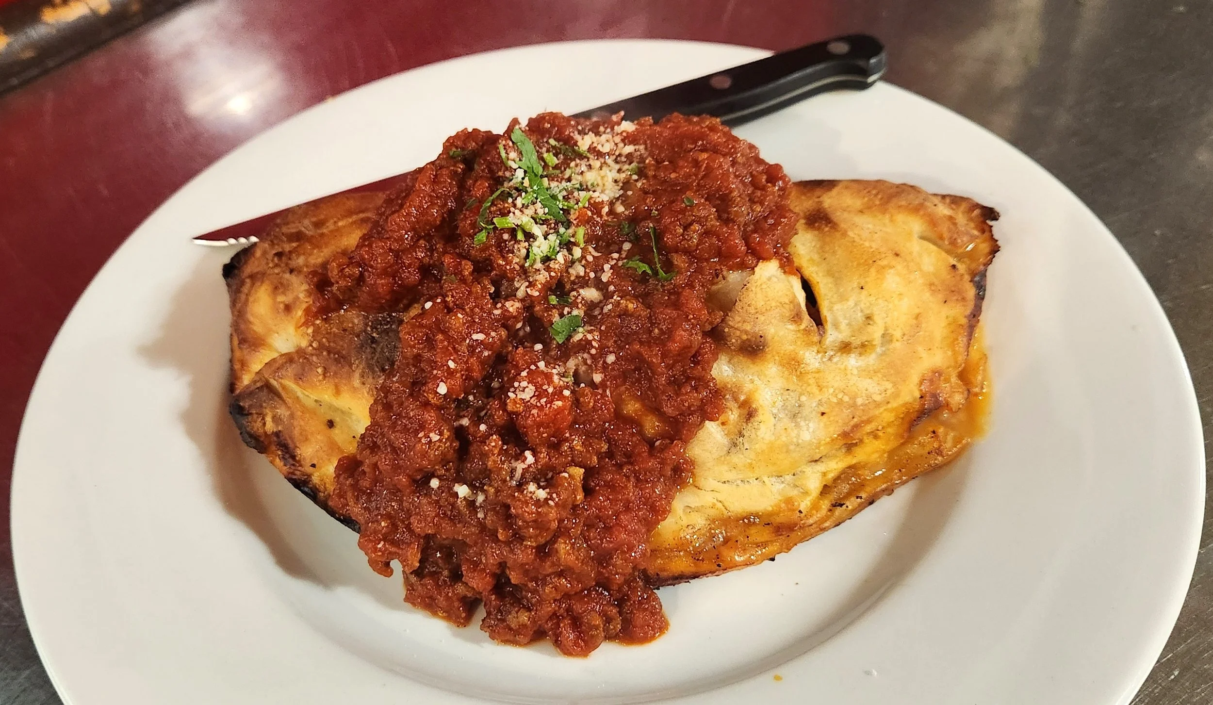 Baked eggplant topped with marinara sauce, grated cheese, and chopped herbs on a white plate.