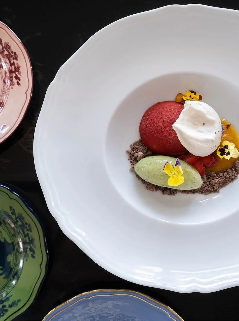 Dessert con pallina rossa, panna, gelato verde, fiori edibili e polvere di cioccolato
