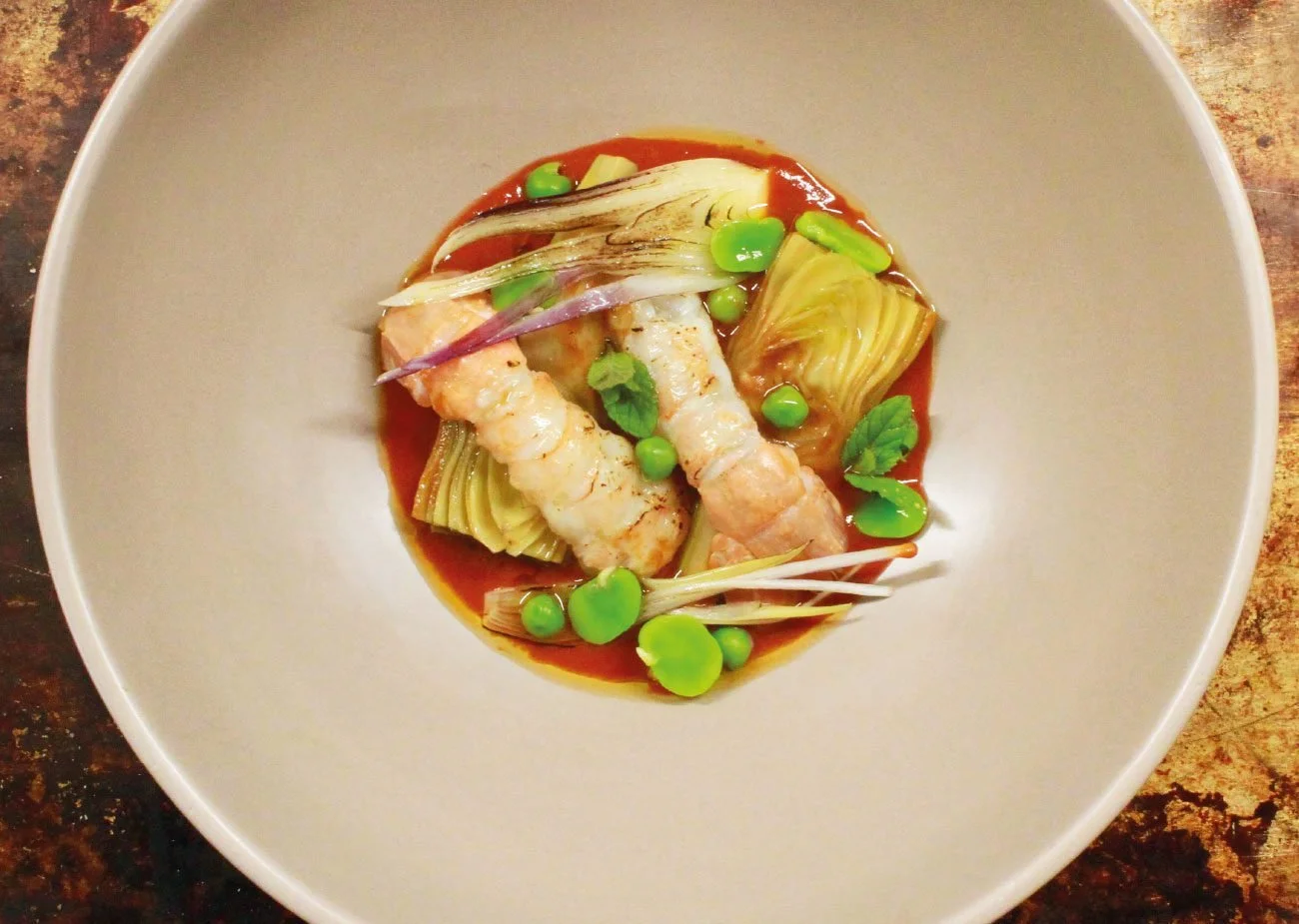 Piatti con gamberi, carciofi, piselli e erbe aromatiche in salsa