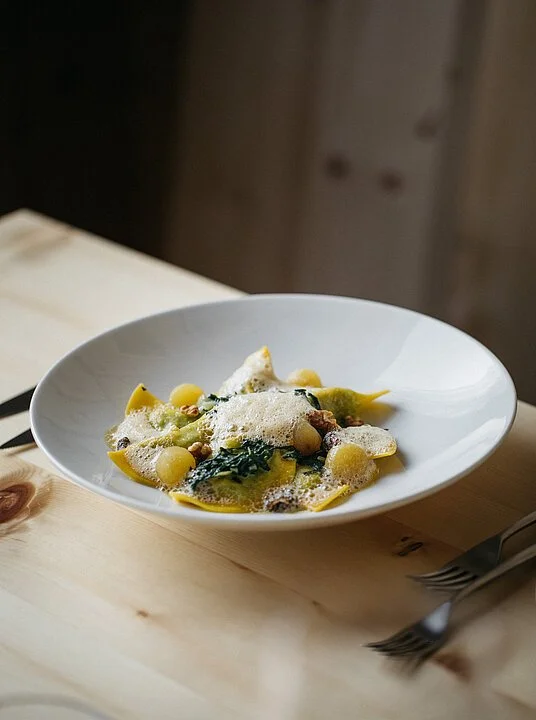 Piatti di pasta ripiena con salsa e formaggio, serviti in una ciotola bianca su un tavolo di legno.