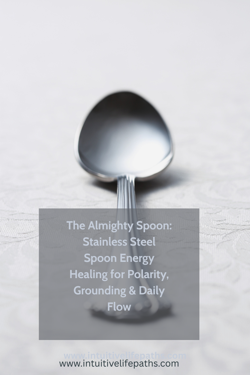 Close-up of a stainless steel spoon on a white lace surface with text overlay: The Almighty Spoon — Stainless Steel Spoon Energy Healing for Polarity, Grounding and Daily Flow — intuitivelifepaths.com