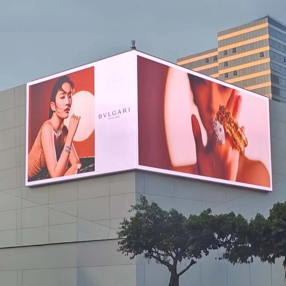 A large outdoor billboard featuring a woman with dark hair and makeup posing with jewelry, next to a close-up image of a hand with multiple large rings, including a diamond ring, advertising BVLGARI jewelry in Dubai.