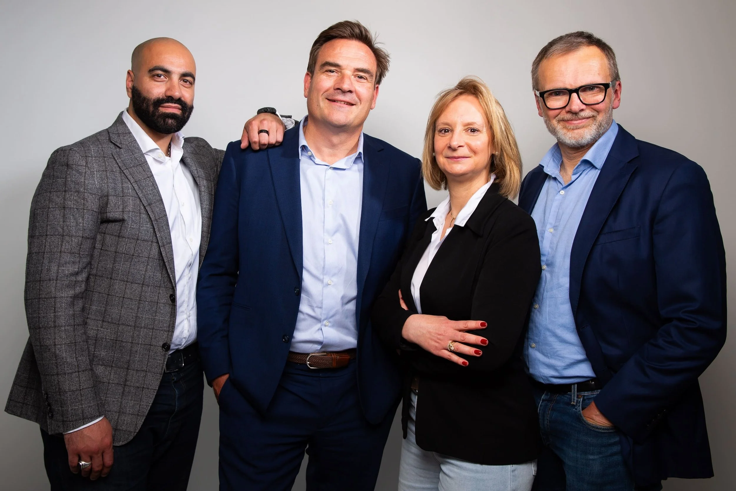 Groupe de cinq personnes, trois hommes et deux femmes, habillées de manière professionnelle, posant pour une photo en intérieur avec un fond gris clair.