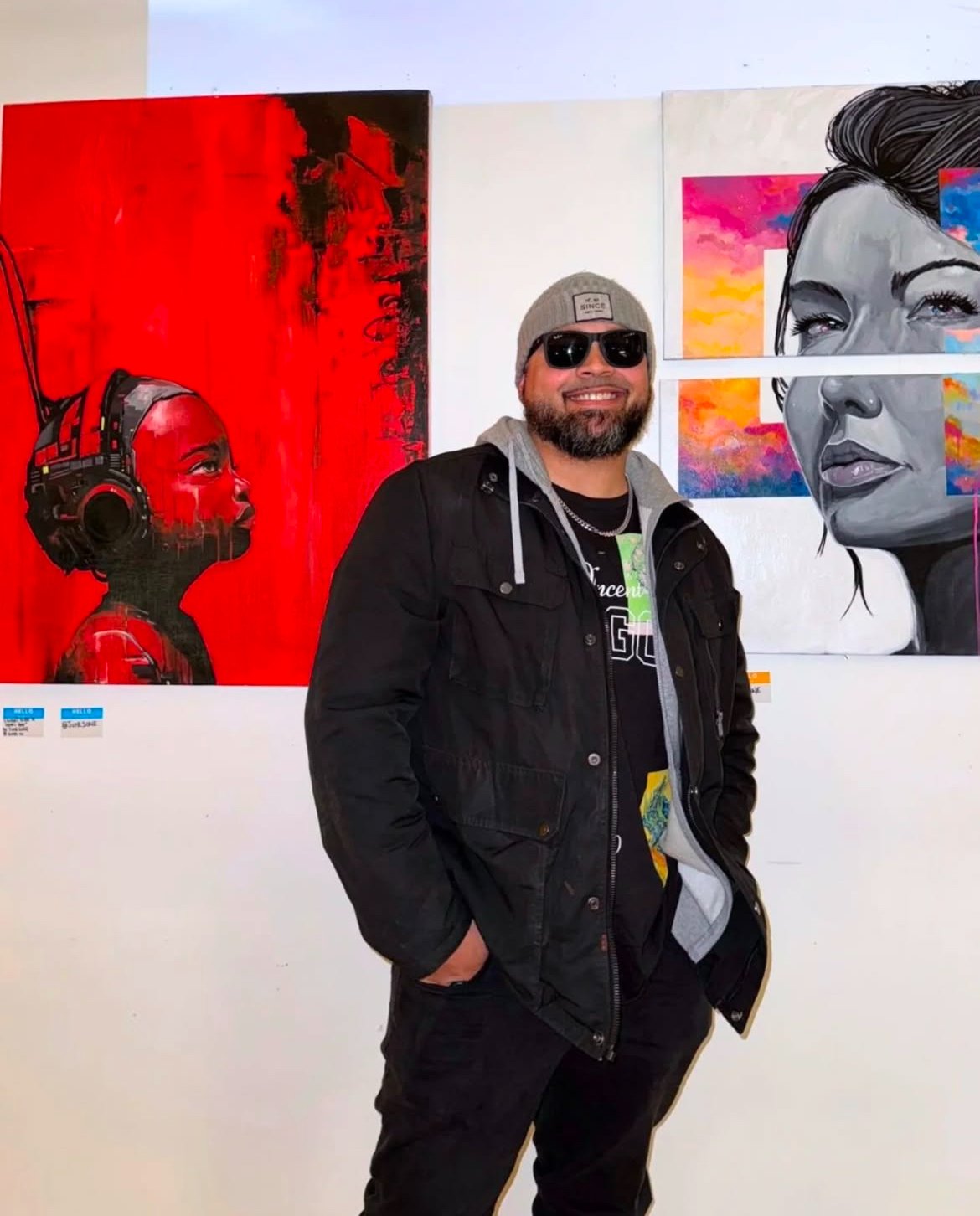 Puerto Rican contemporary artist June1one at an art exhibition, standing before colorful original artwork.
