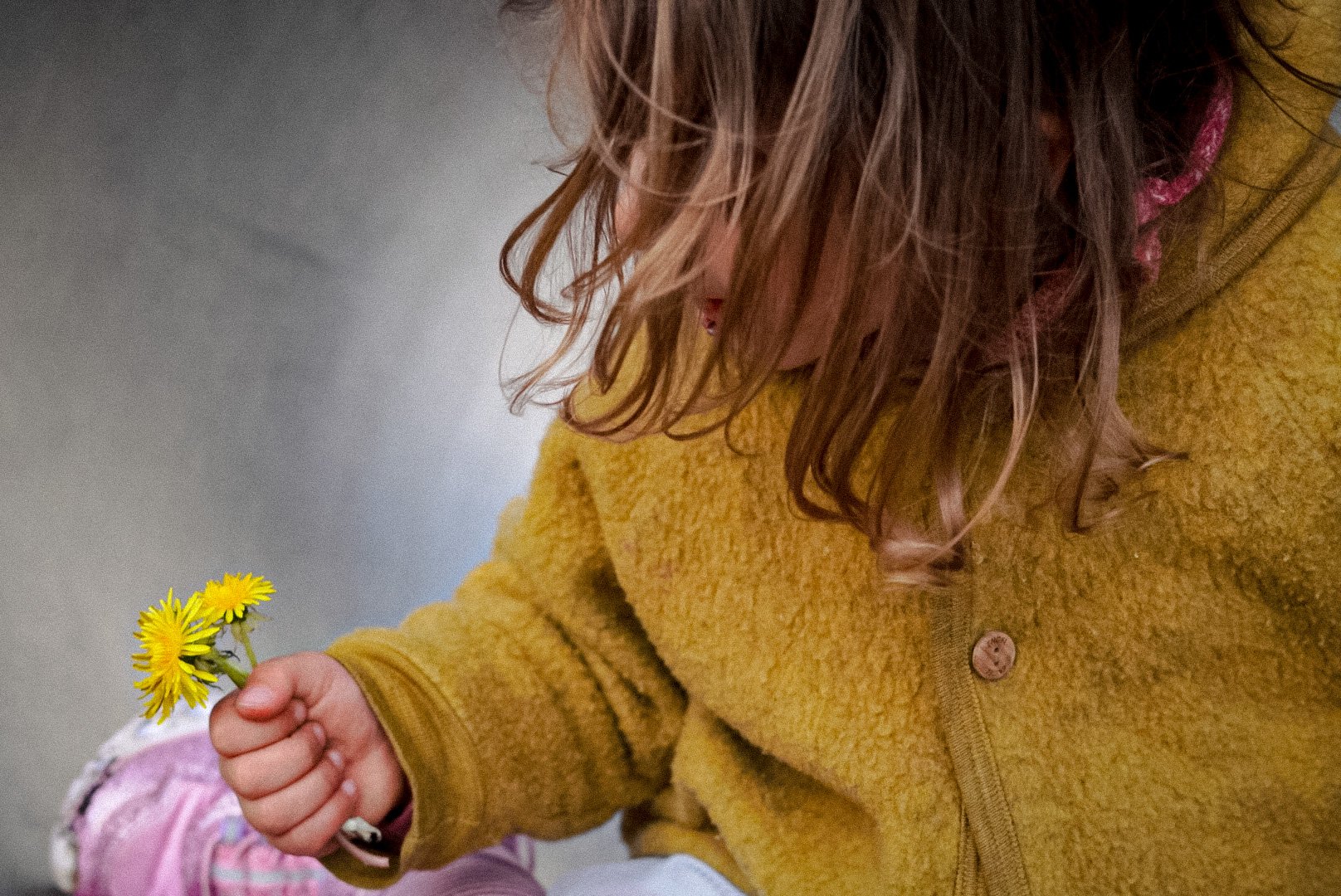 Frau in gelber Jacke hält eine kleine gelbe Blume in der Hand.