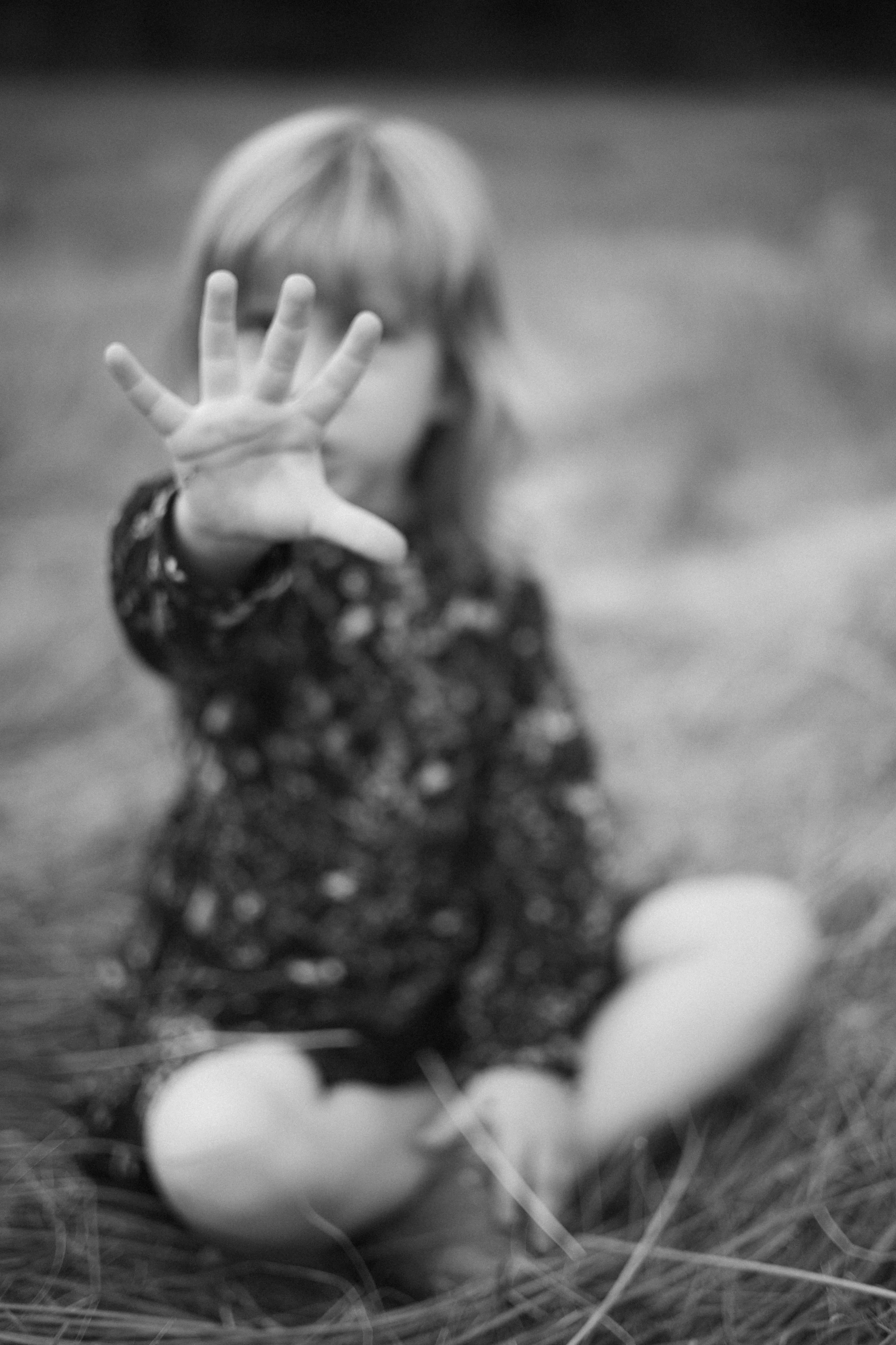 Junge Frau sitzt im Gras, hebt die Hand zur Kamera, Gesicht unscharf, Hintergrund unscharf, Schwarzwald-Stil, schwarz-weiß.