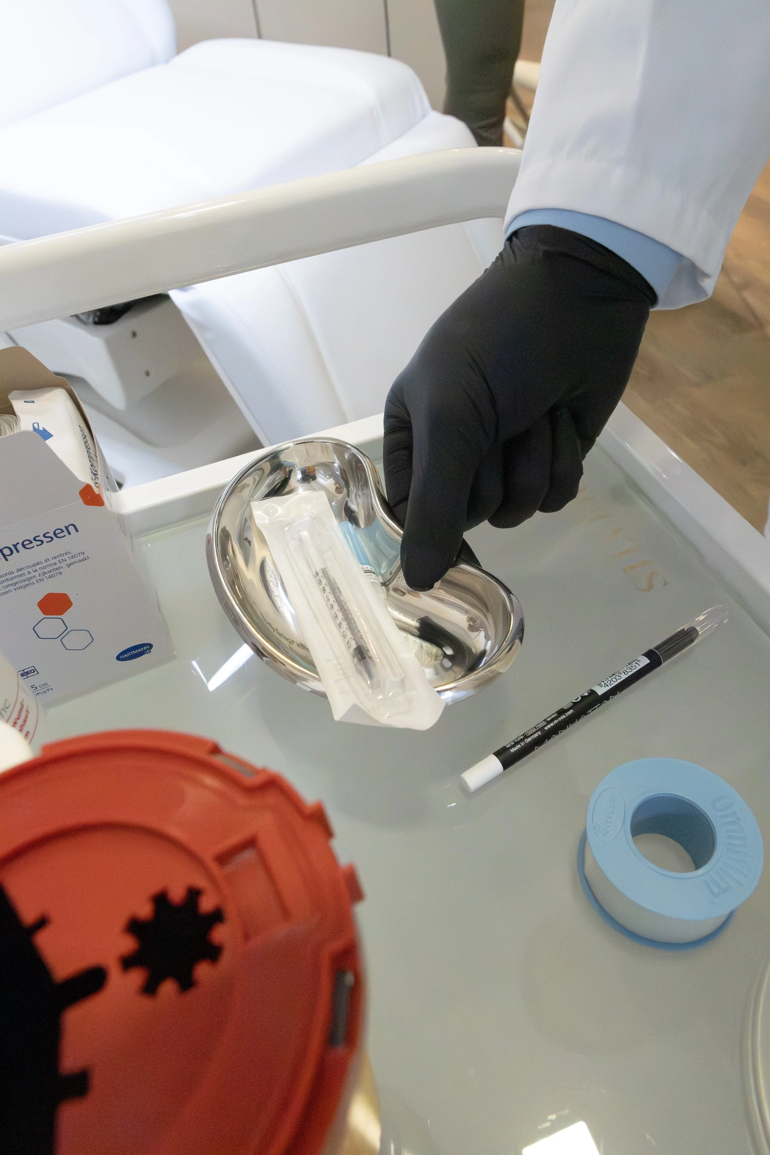 Ein Arzt oder medizinisches Personal in schwarzer Handschuhen bereitet einen Injektionsspritzen vor, die auf einem sterilem Tablett liegt, in einem medizinischen Raum.