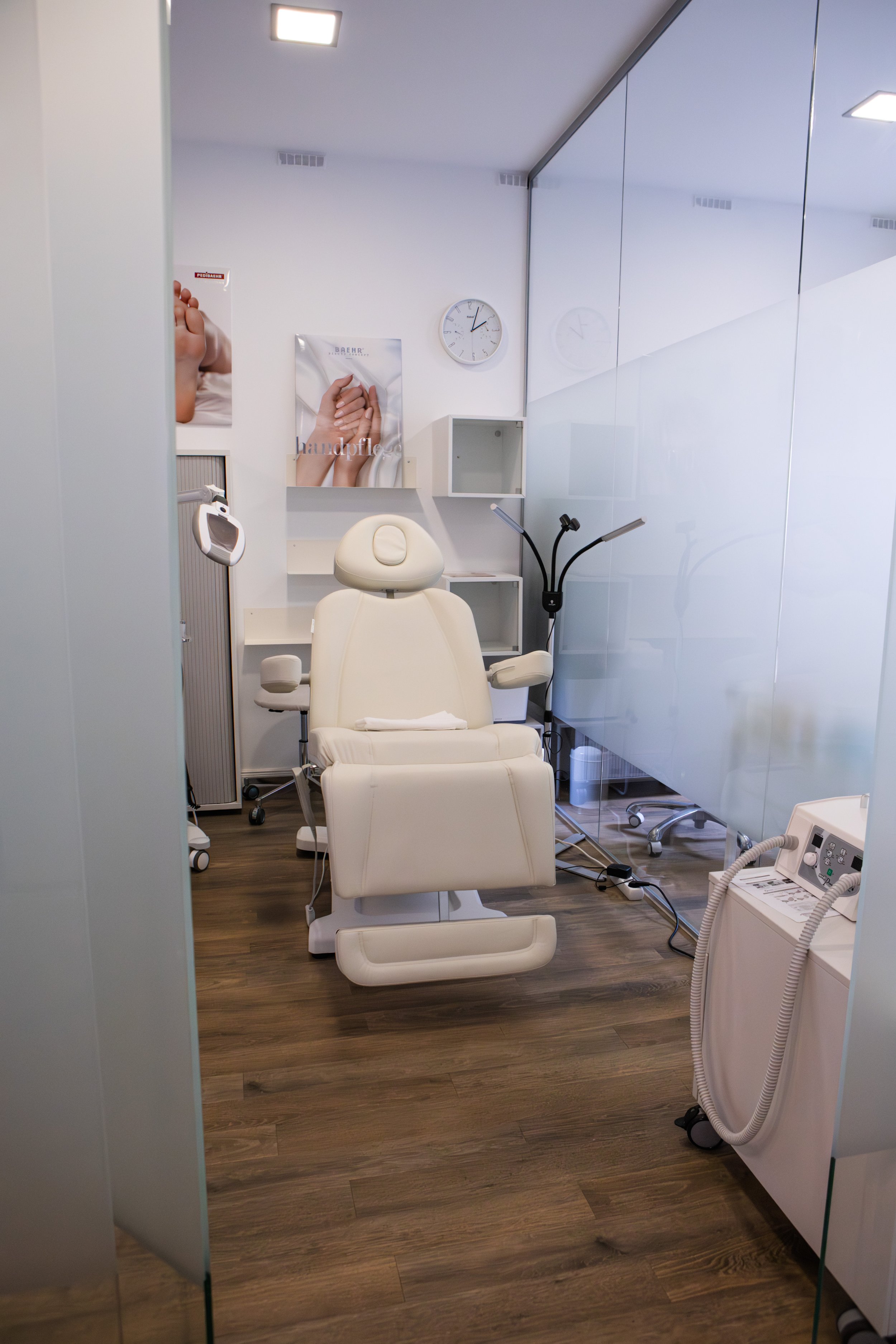 Ein schön eingerichteter Behandlungsraum in einer Klinik, mit einem weißen Lehnstuhl in der Mitte, einem medizinischen Gerät auf der rechten Seite, und einem Poster mit Händen, die gehalten werden, an der Wand im Hintergrund.