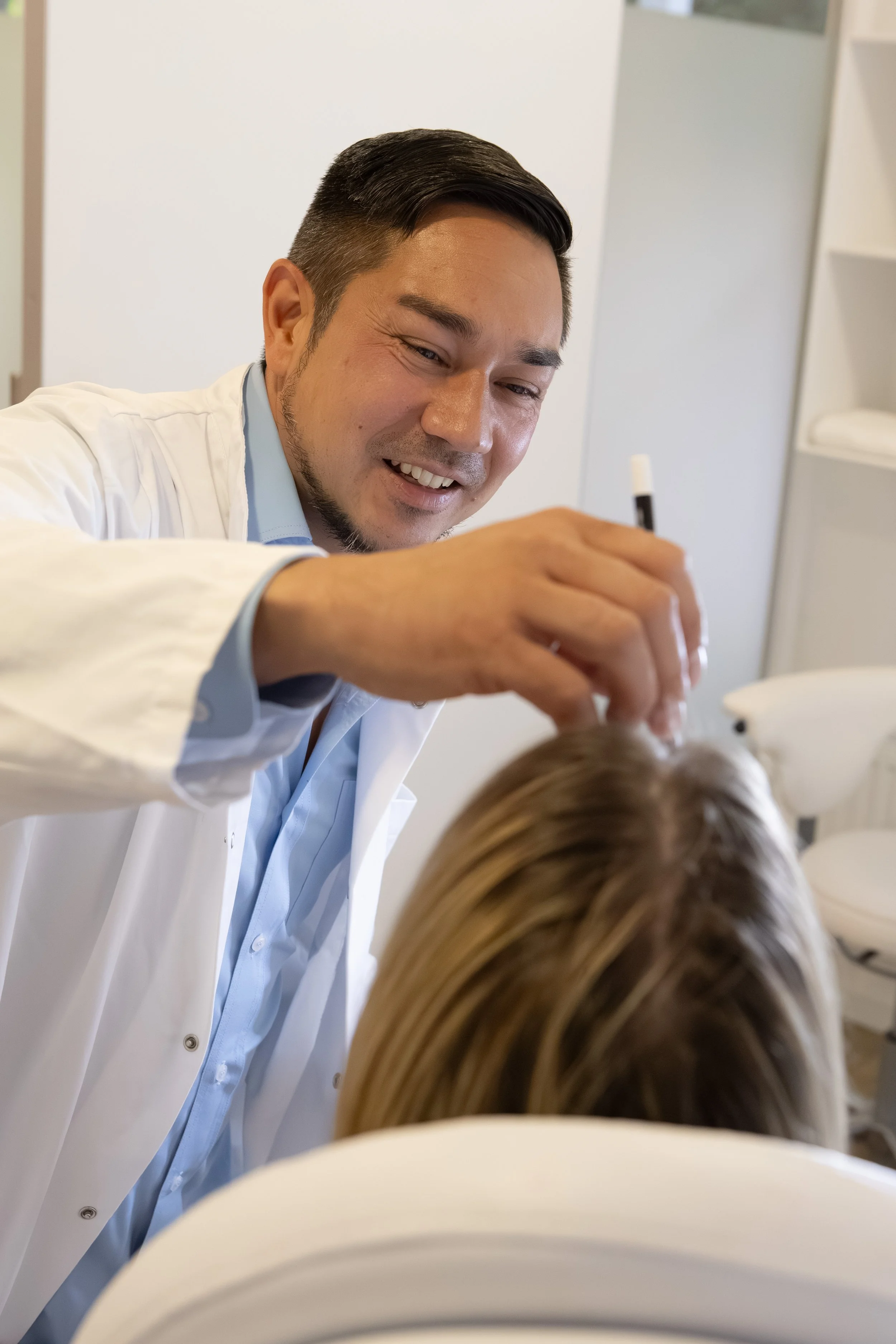 Ein männlicher Arzt in einem weißen Kittel tätigt eine medizinische Untersuchung an einer Patientin, die auf einer Untersuchungsliege liegt, in einer Arztpraxis.
