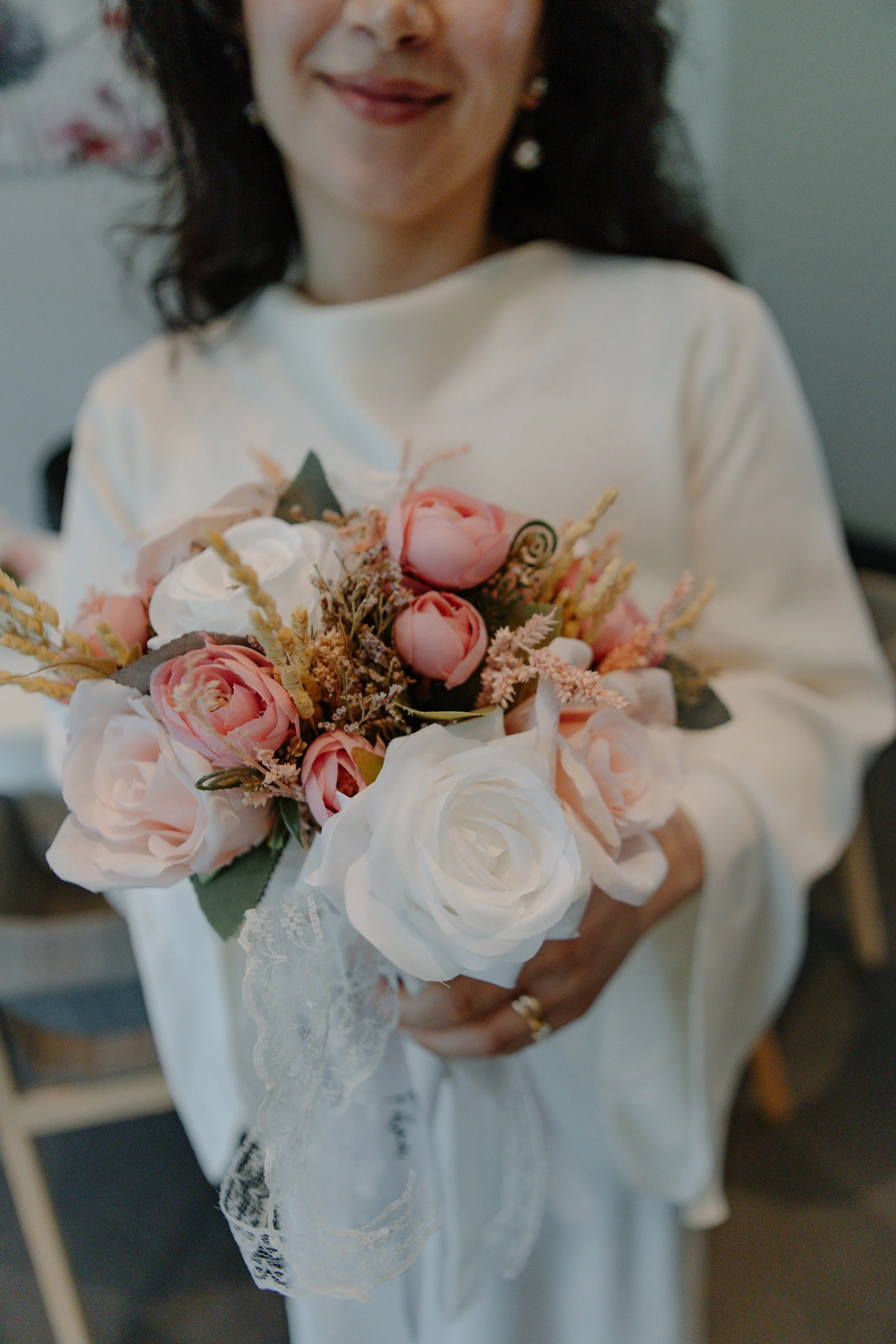 Frau hält einen Brautstrauß mit weißen und rosa Blumen, verziert mit Spitze.