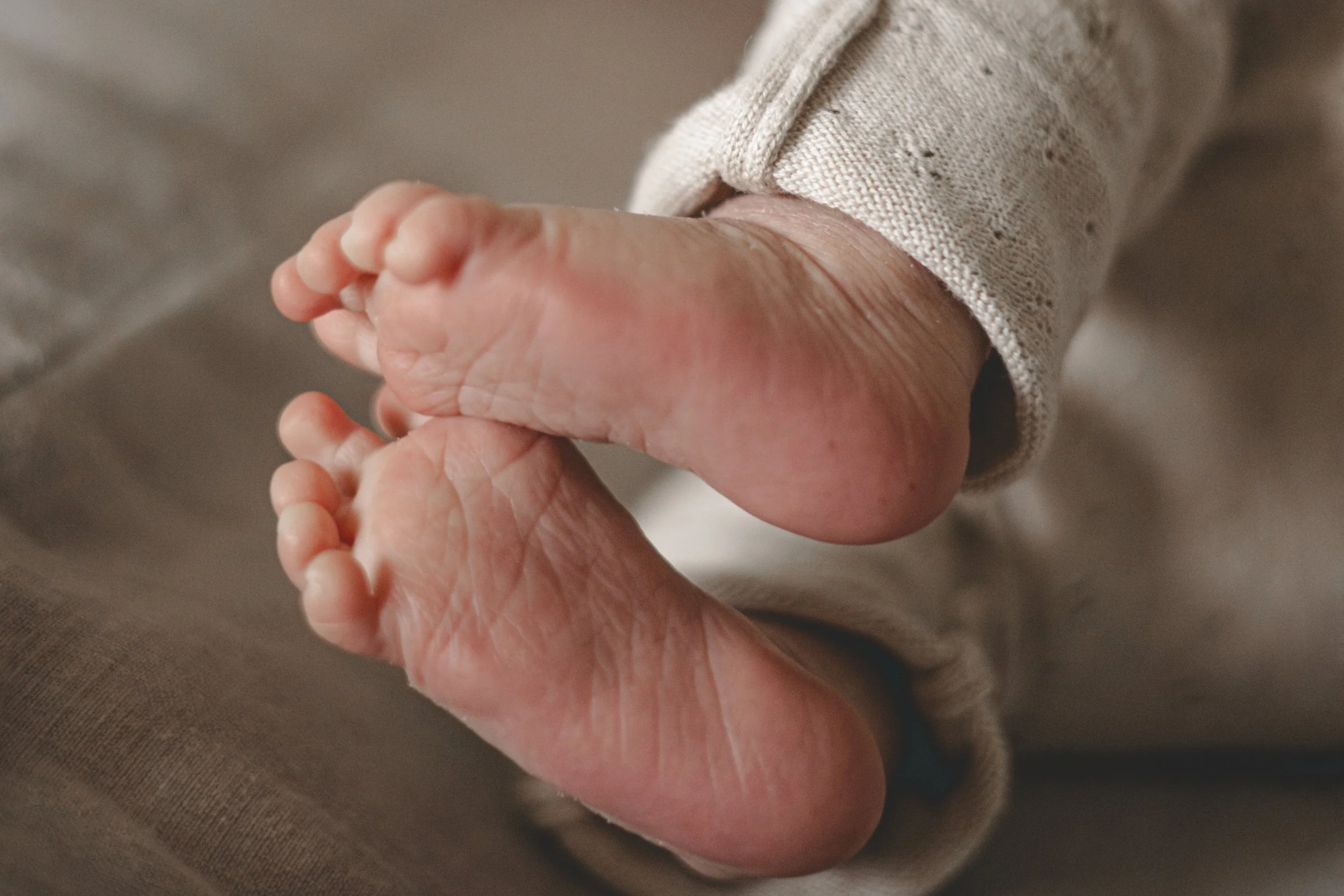 Nahaufnahme der kleinen Füße eines Babys, eingekleidet in beige Kleidung.