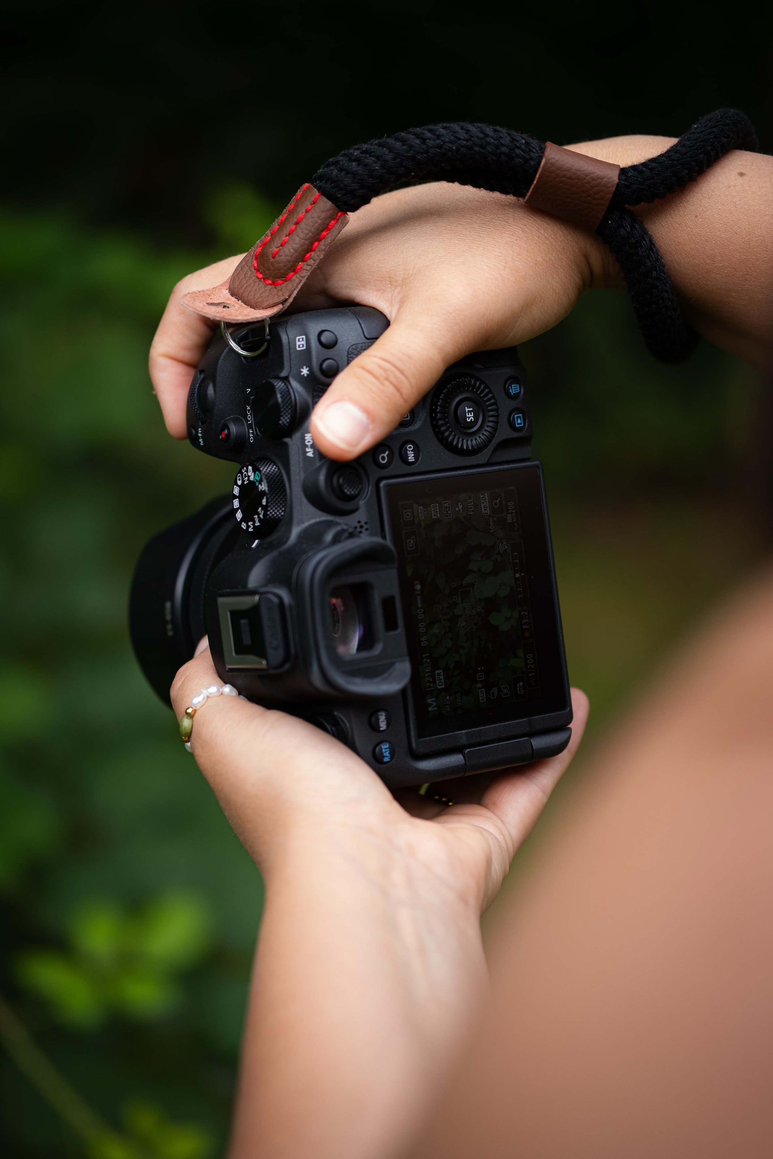 Nahaufnahme einer Person, die eine DSLR-Kamera hält, mit Fokus auf die Kamera und die Hände. Hintergrund unscharf.
