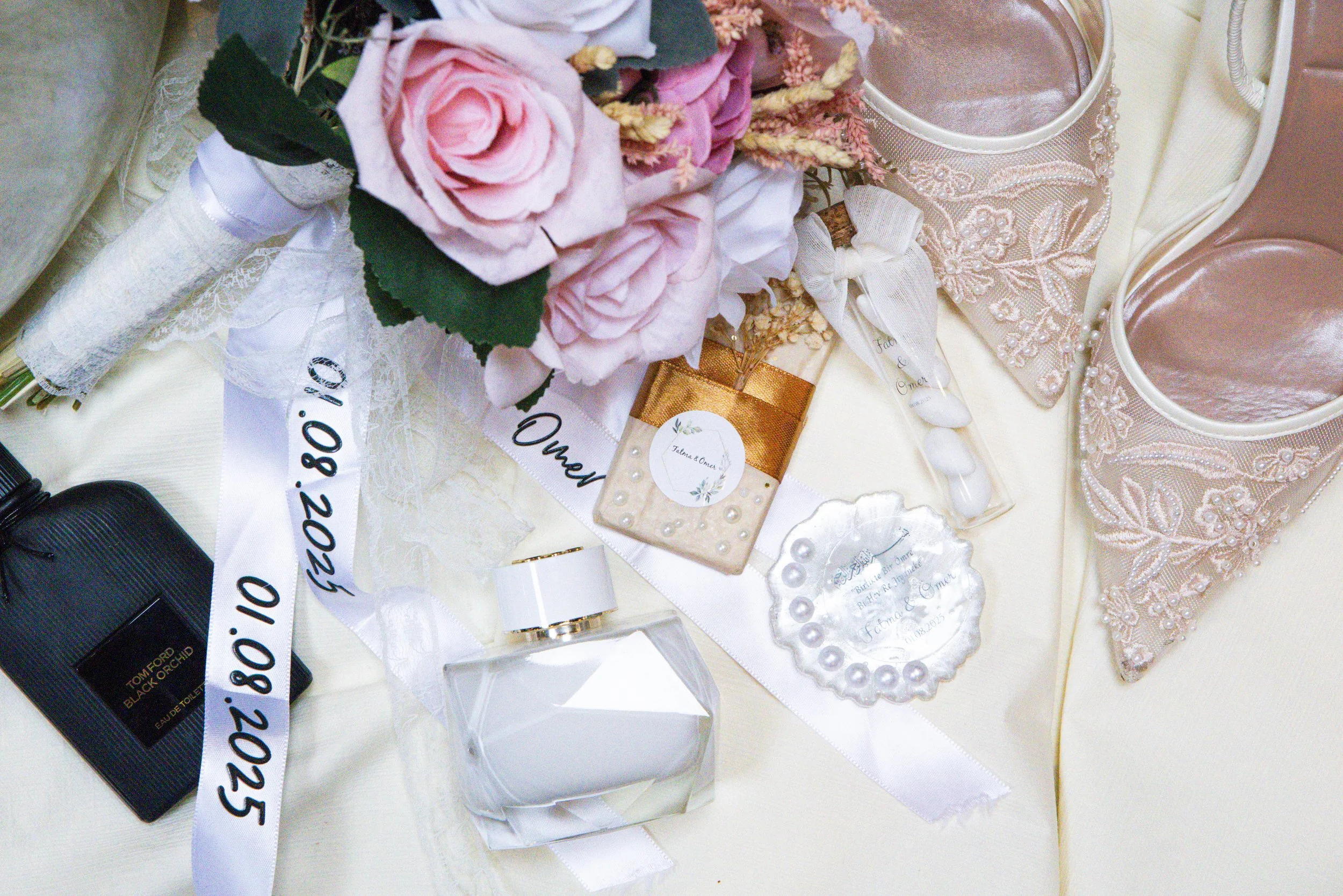 Hochzeitsdekoration mit Blumen, Parfüm, Kerzen, Schmuck und Anhängern in Pastellfarben und Goldakzenten auf einer Tabelle.
