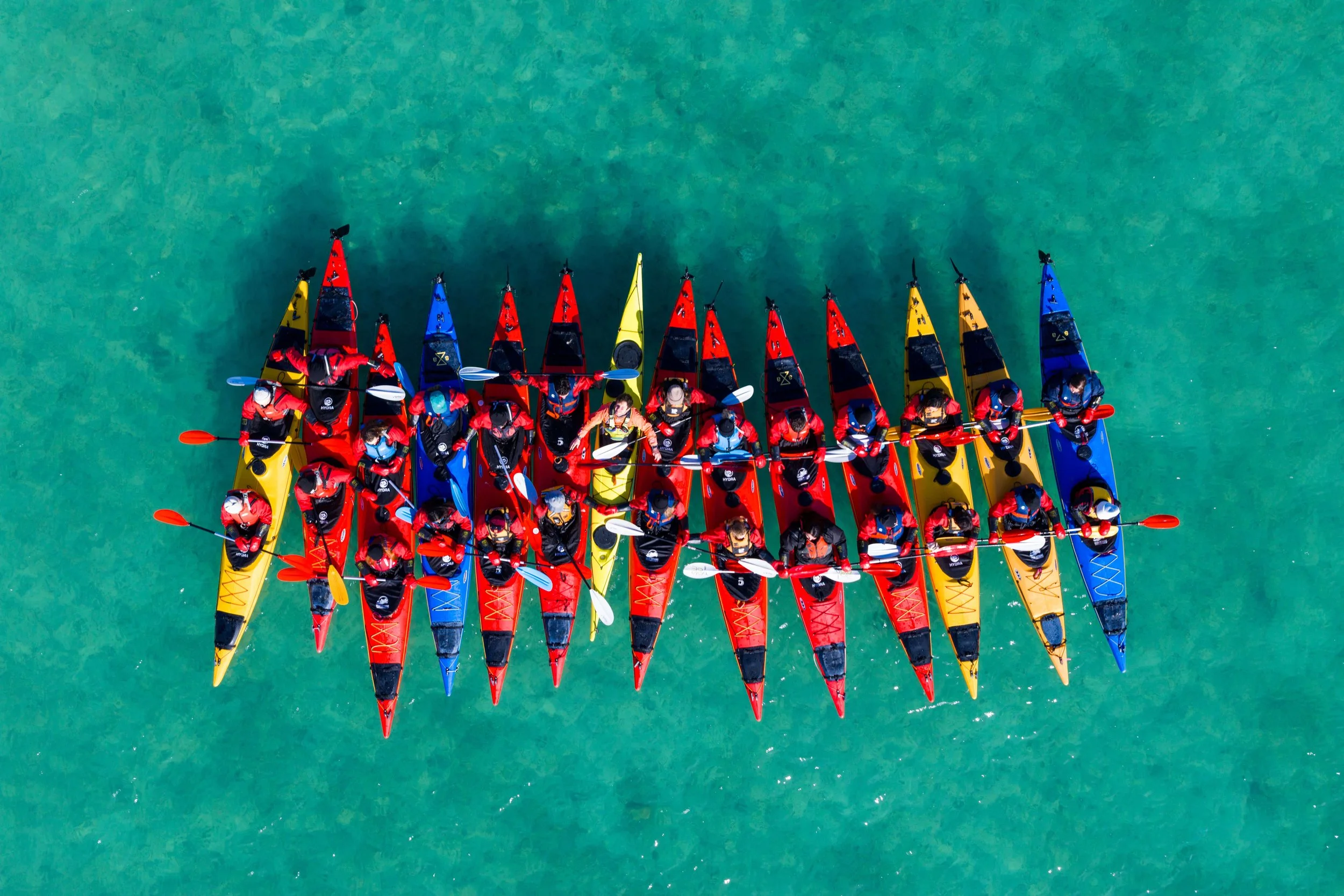 Colorful kayaks on a sandy beach, with water and mountains in the background under a partly cloudy sky.