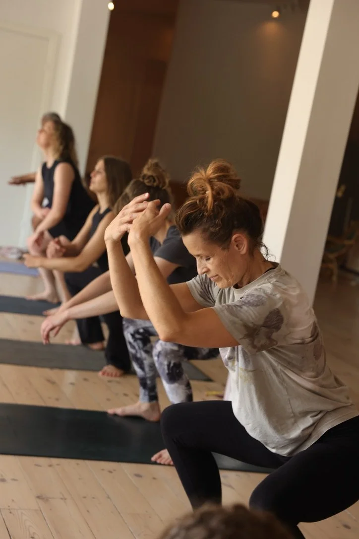 Kvinder på yogaundervisning, der sidder i en skyttegravstilling og øver åndedrætsøvelser.