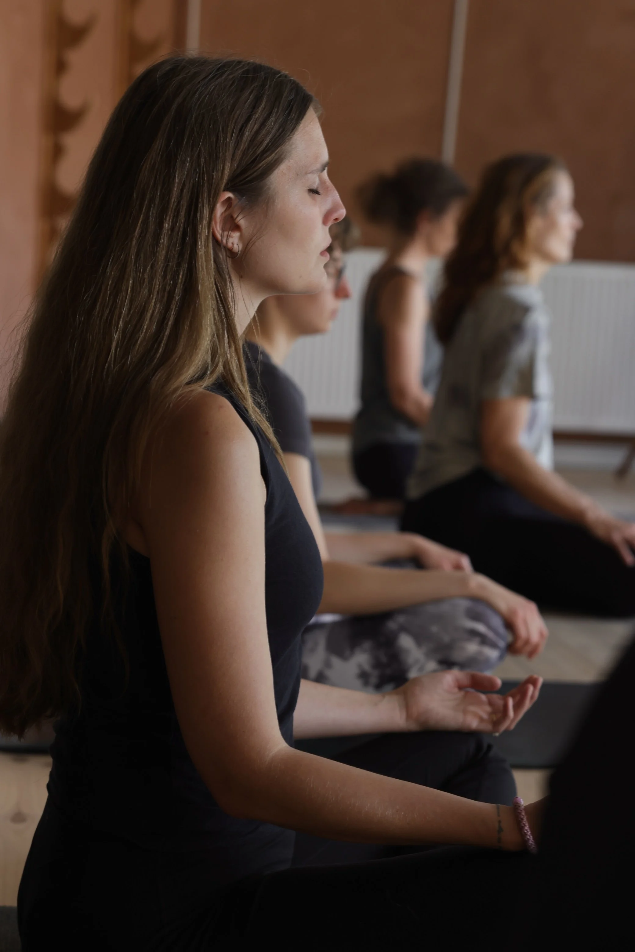 En gruppe kvinder sidder i meditationsstilling med lukkede øjne i et roligt rum.
