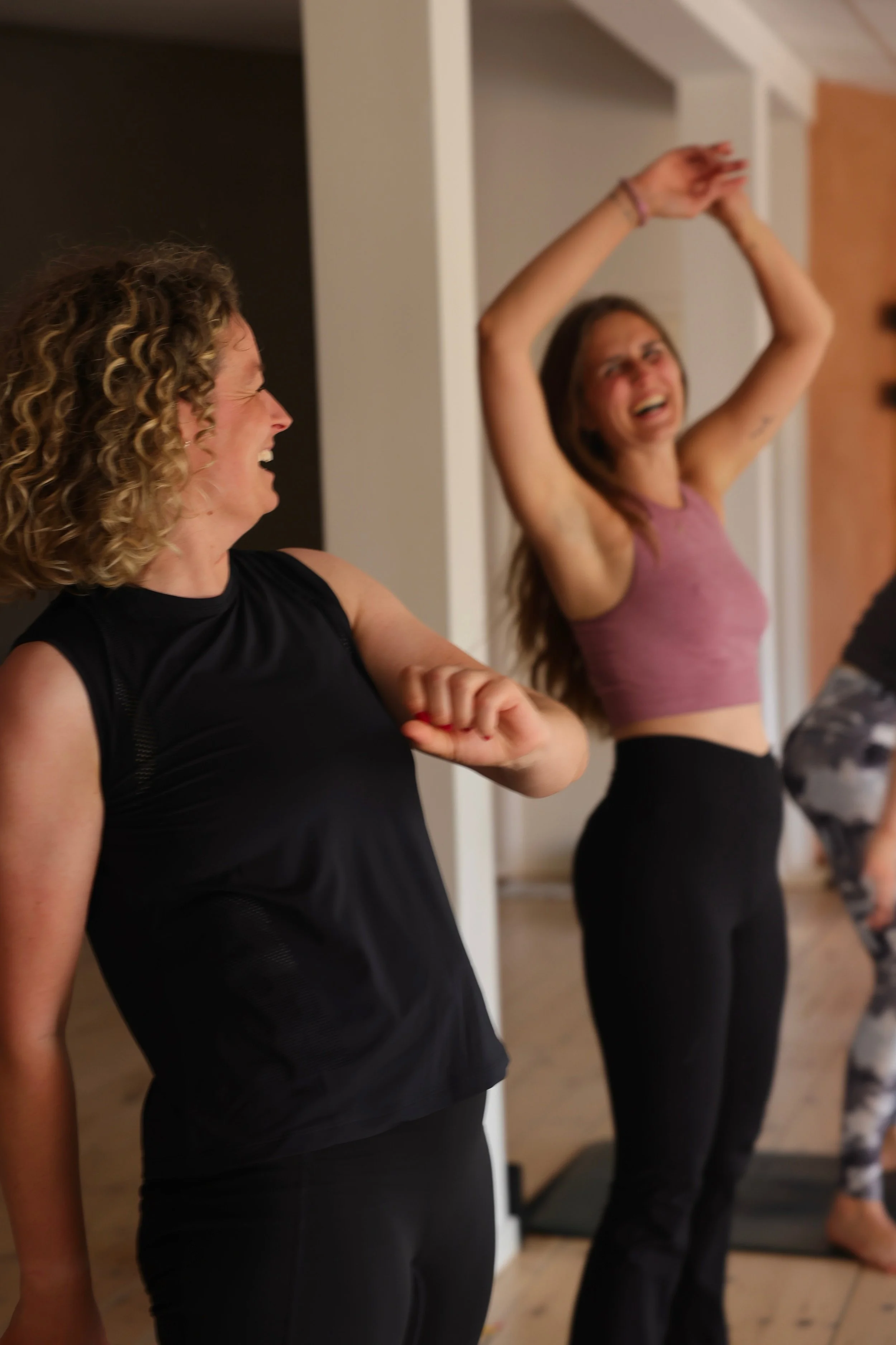 To kvinder i træningsbeklædning ler og har det sjovt under en fitnessklasse.