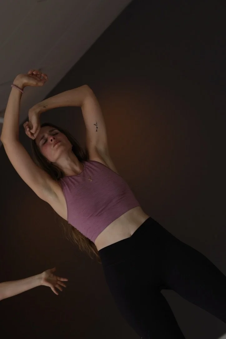 En kvinde i en sporttop, der strækker sine arme op over hovedet, med et begrænset syn på et værelse.