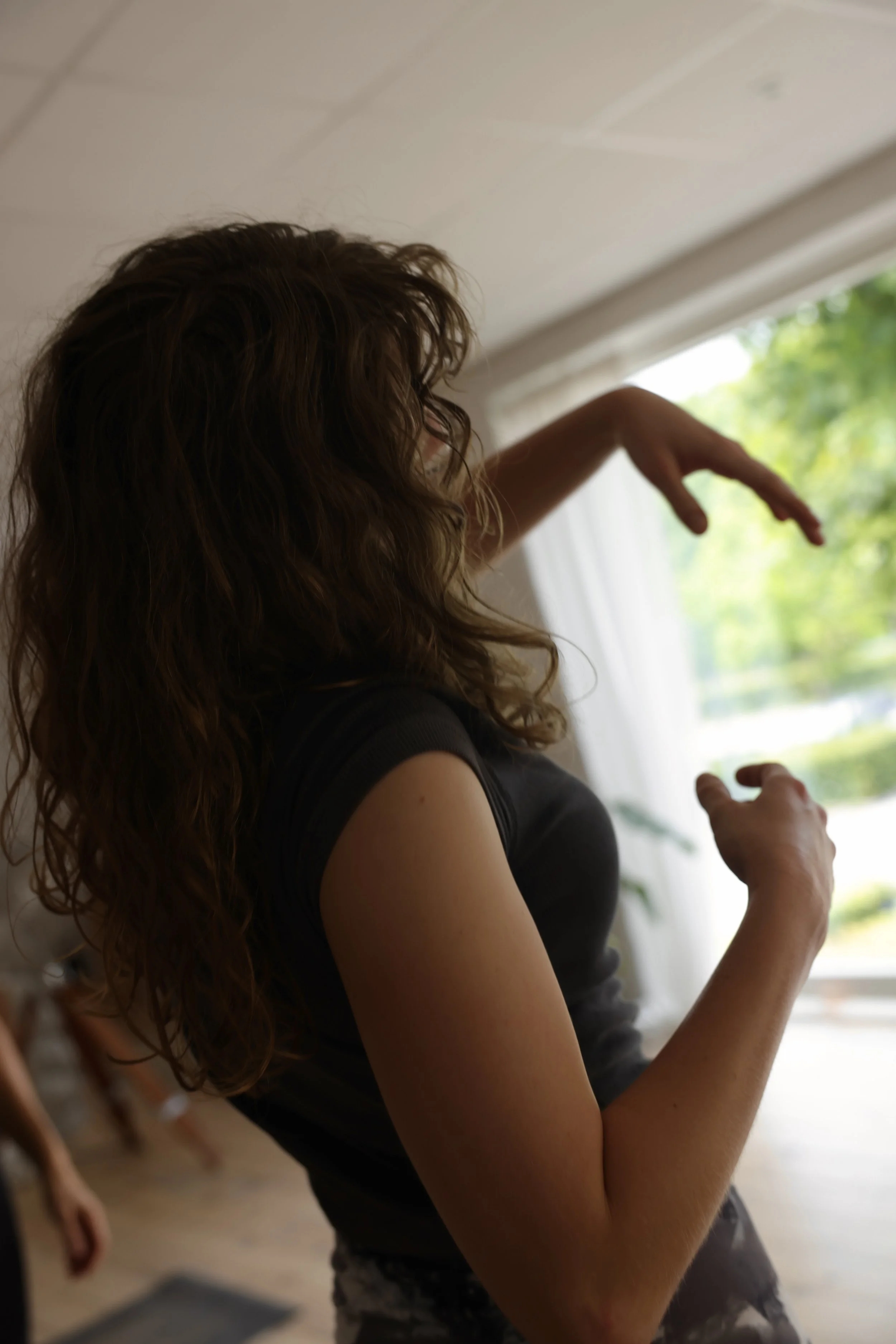 Kvinde med brunt, bølget hår står ved et vindue og kigger ud.