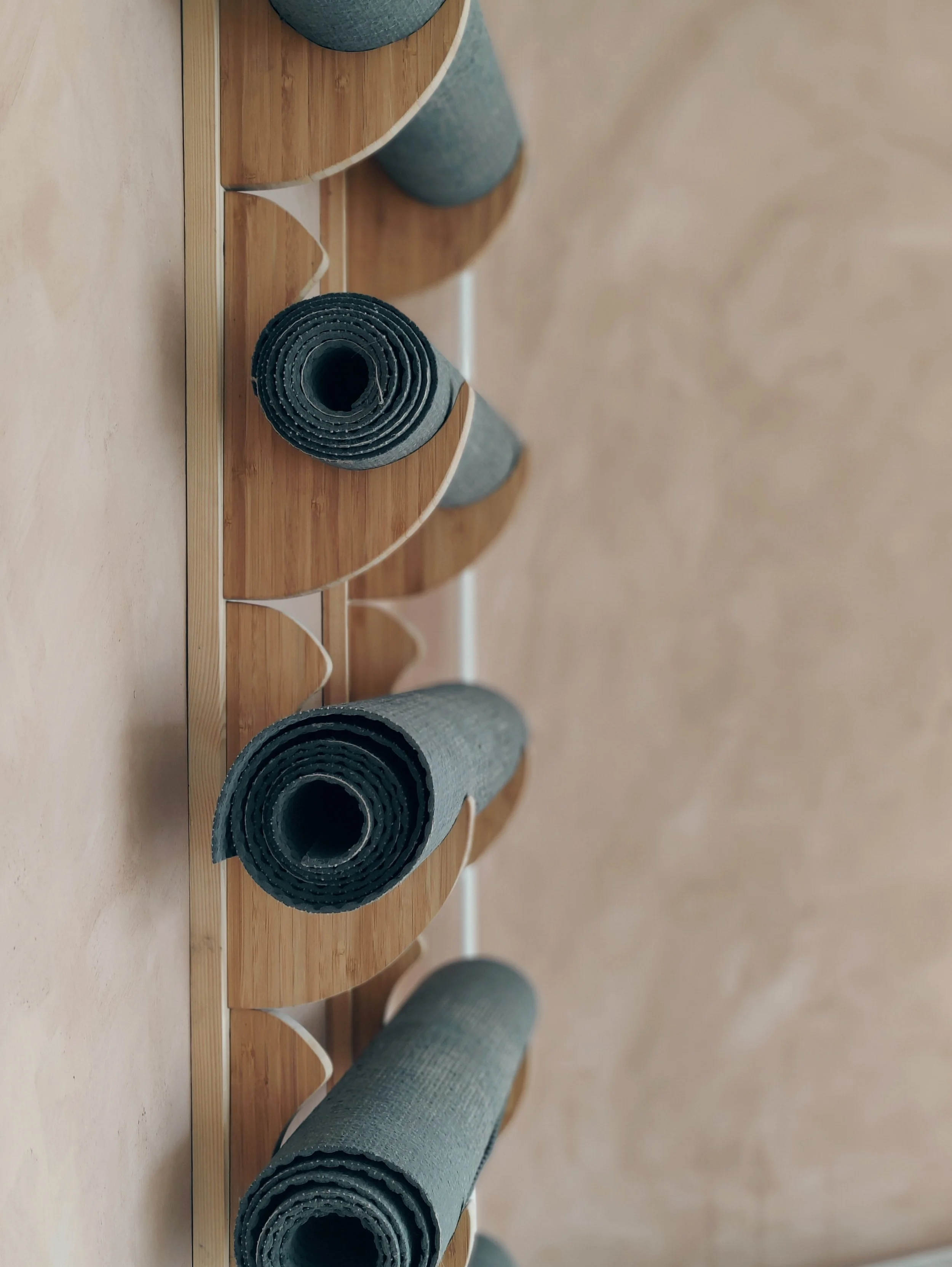 Fire rulle yoga- eller fitnesstæpper i forskellige nuancer af grå, placeret på en træhylde.