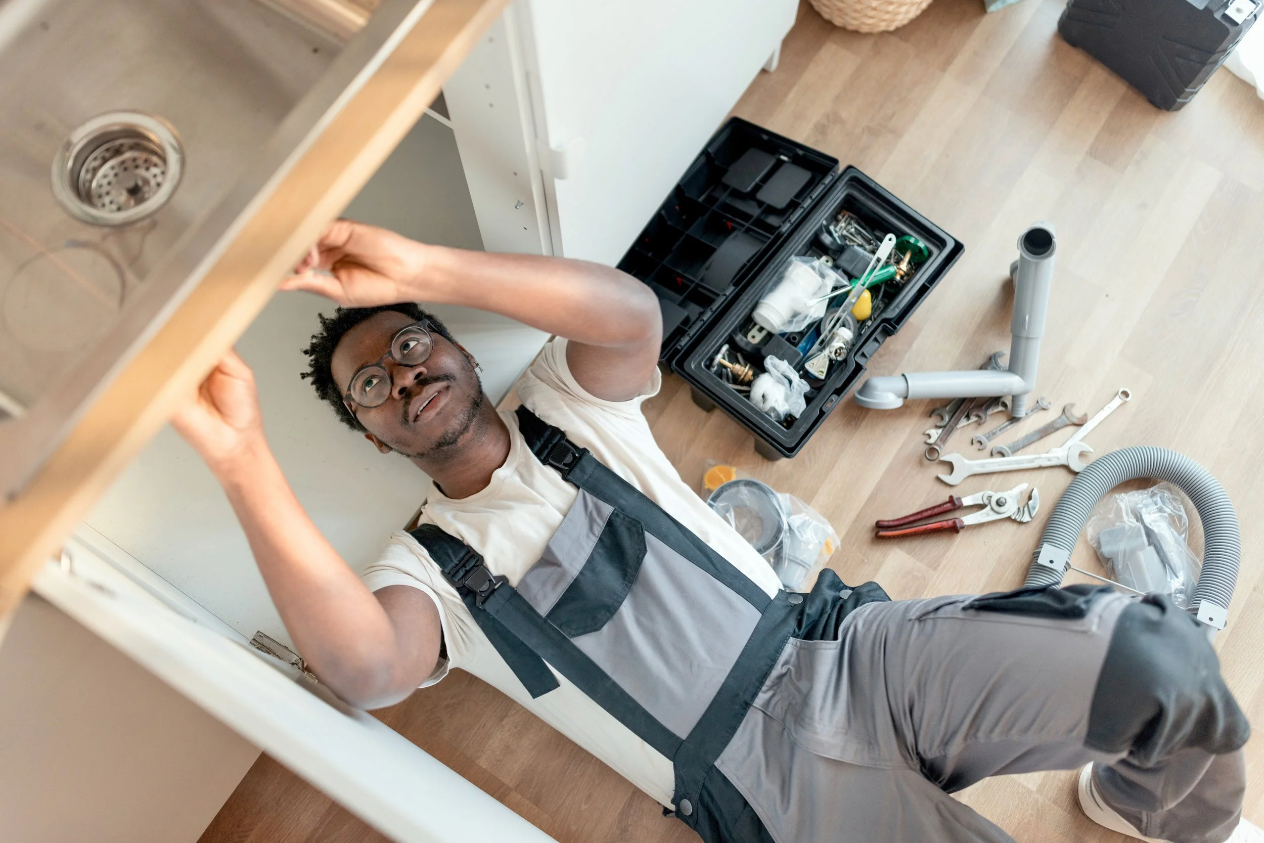 Man installing or repairing under sink plumbing, tools and parts scattered on the floor.