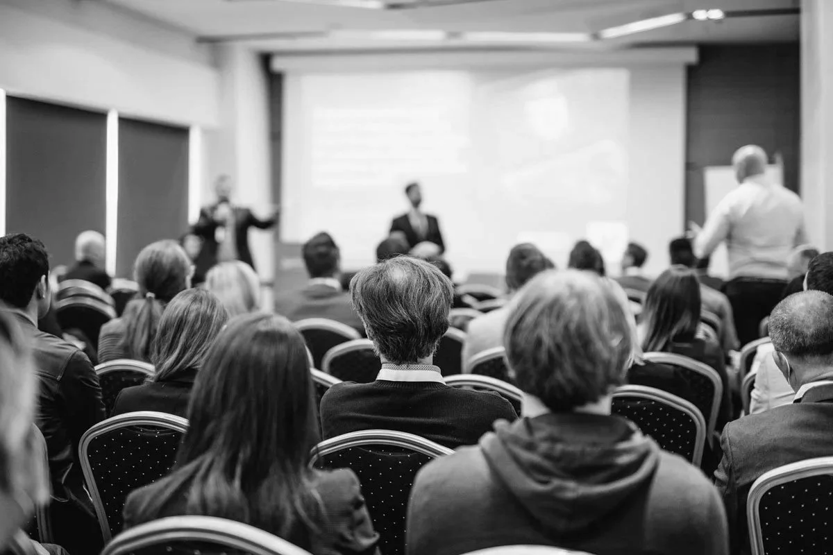 Persone sedute in un'aula di conferenze che ascoltano un relatore in piedi davanti a un proiettore.