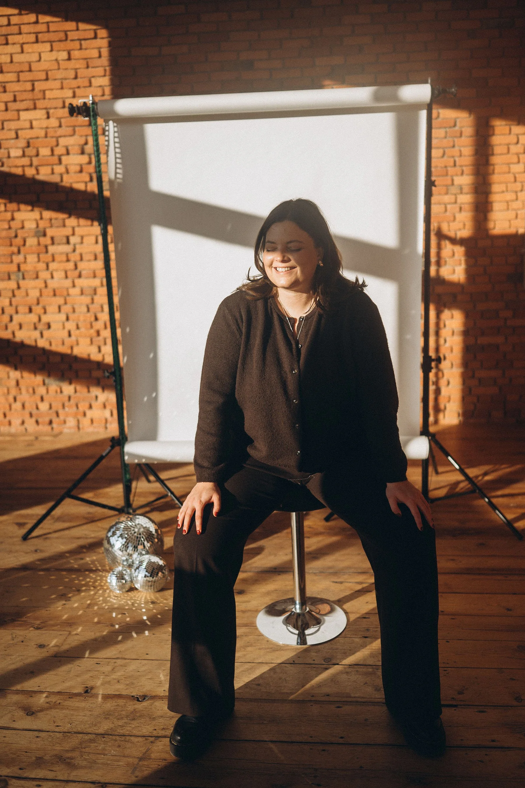 a portrait of shauni in the studio with a white canvas behind her and discoballs on the floor