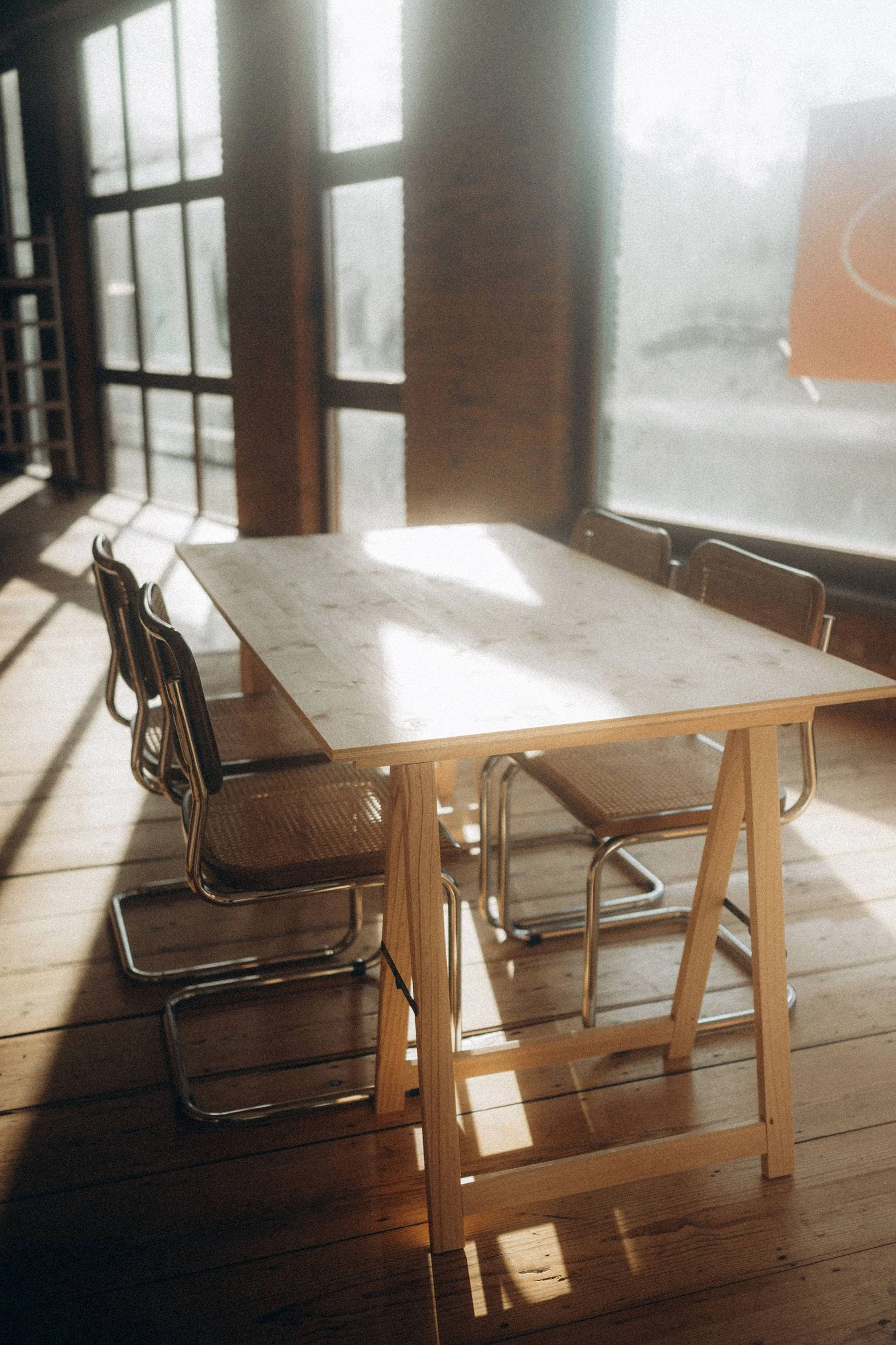 a table with chairs with sunlight coming in and a lot of windows