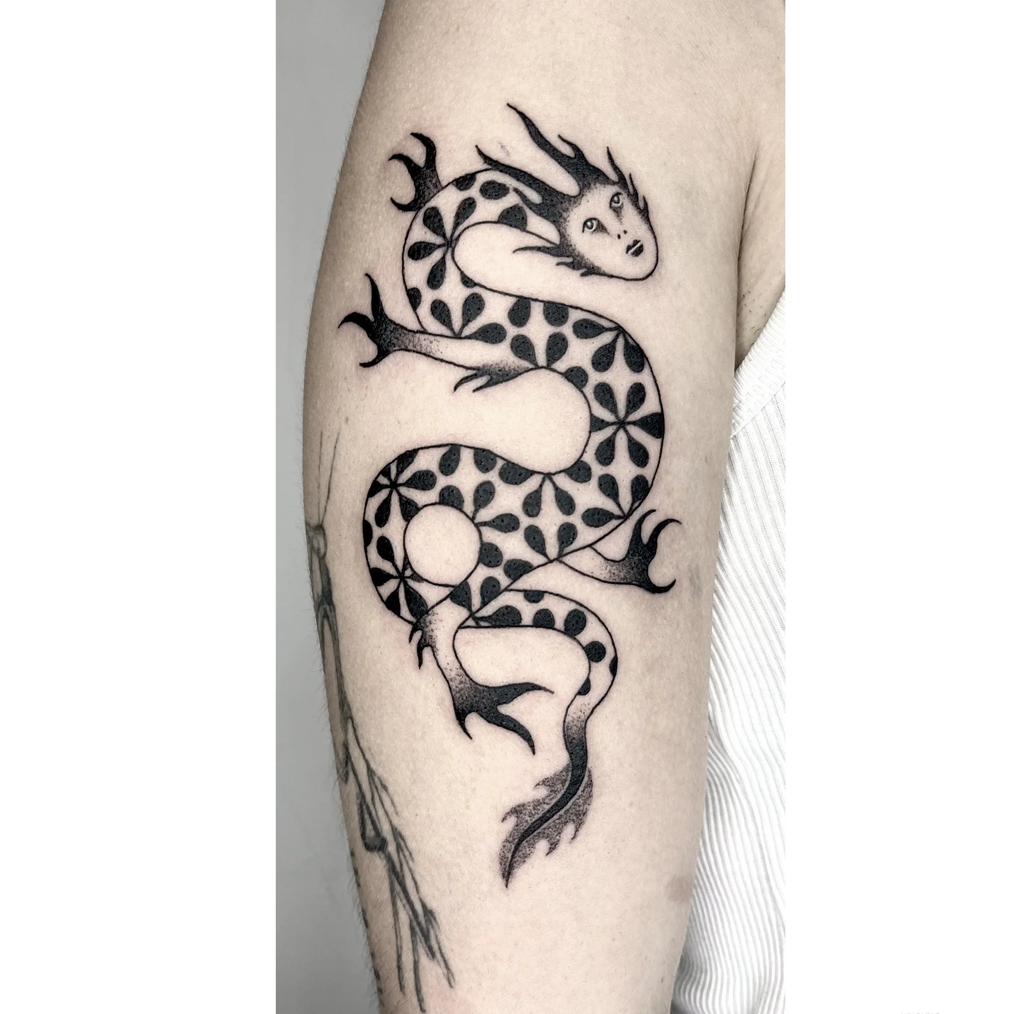 Tattoo of a dragon with a woman's face and floral pattern on body
