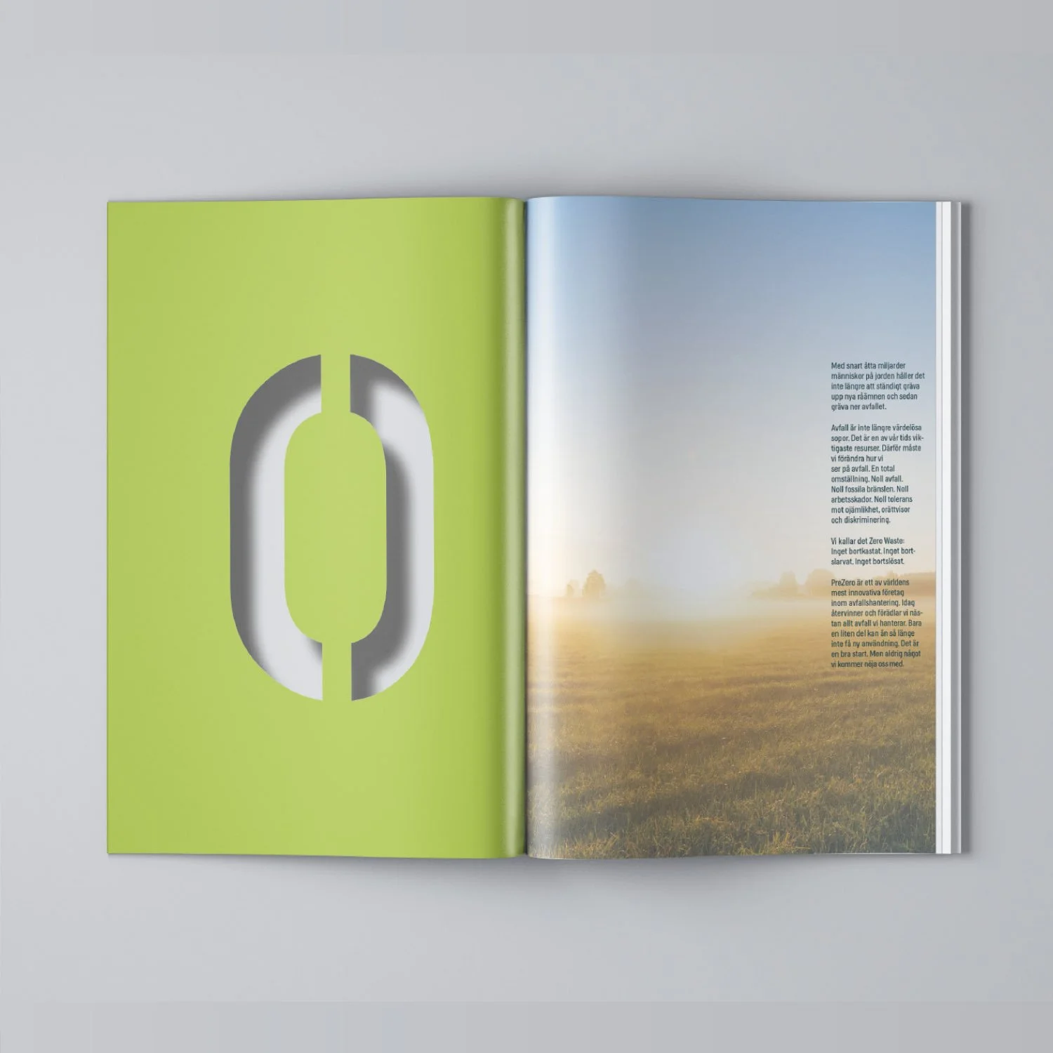 Open magazine displaying a large green page with a cut-out of a zero and a page with a field of grass and trees at sunrise or sunset.