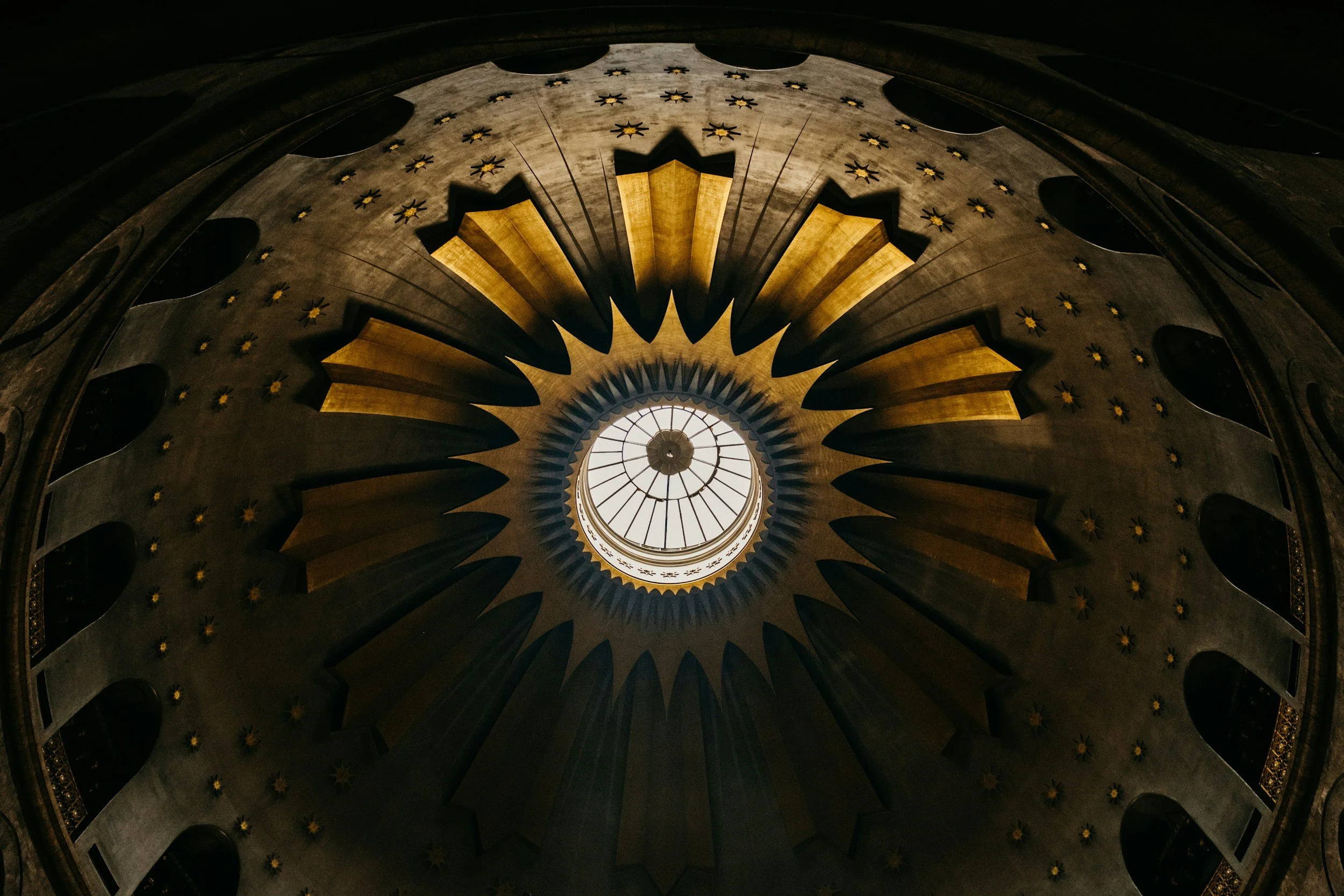 Looking up at the ornate ceiling of a building with a central skylight and decorative elements.