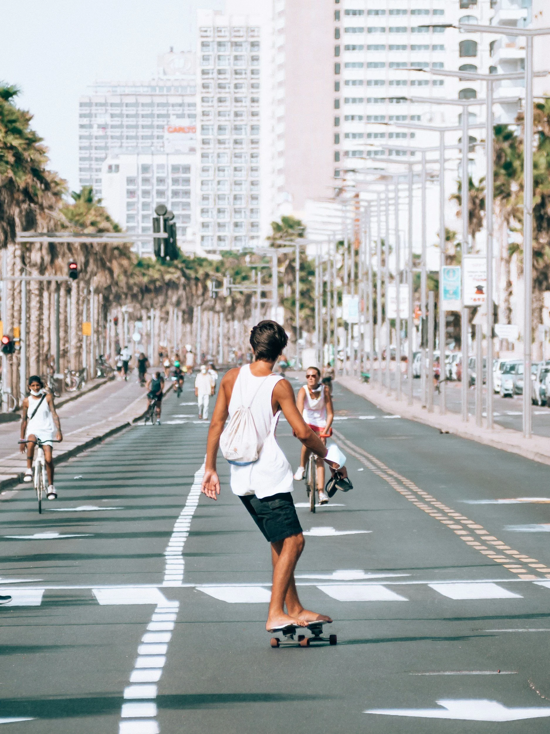 Person skateboarding on a city street with people cycling, walking, and tall buildings in the background.