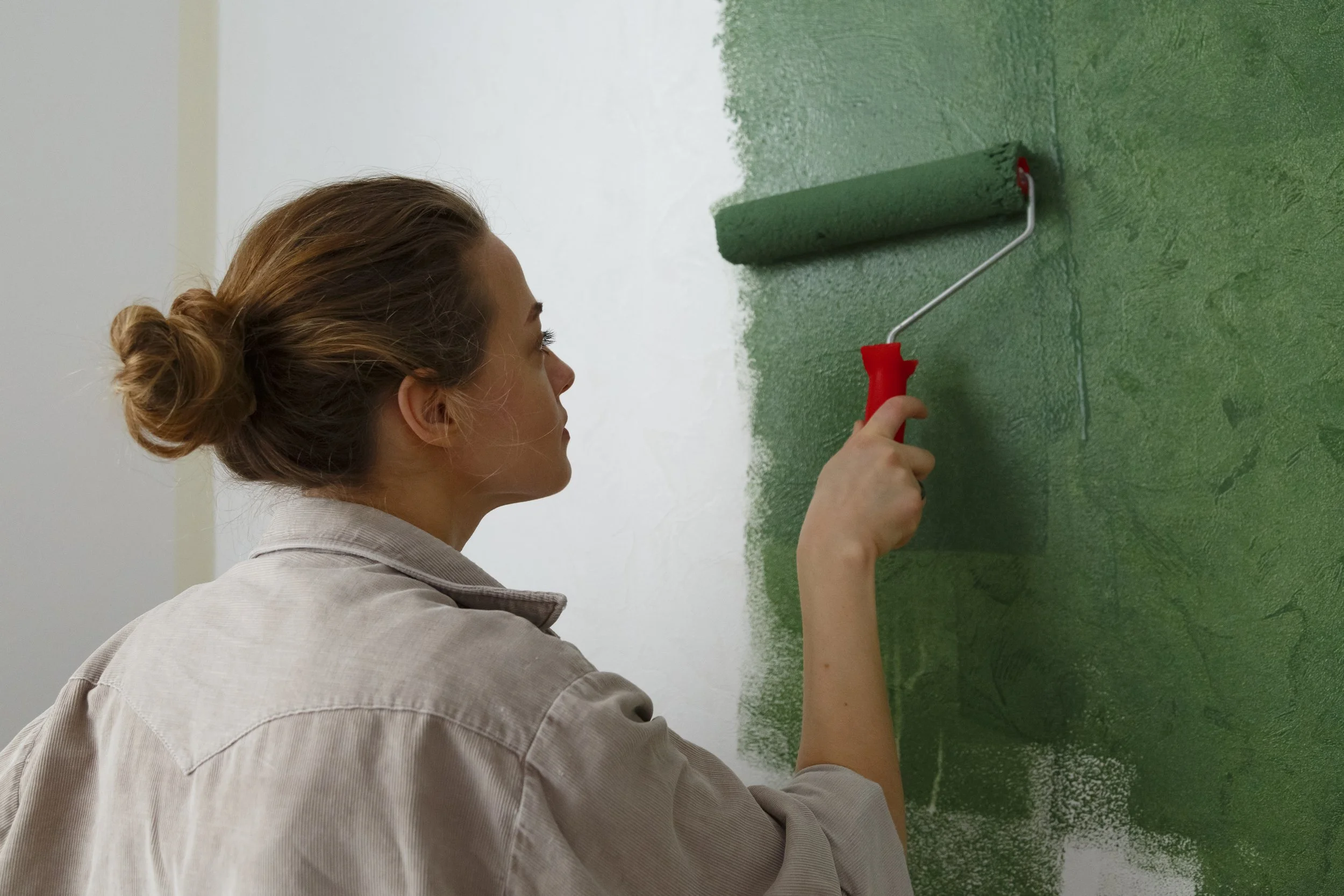 Vue de derrière d’une jeune femme appliquant au rouleau de la peinture verte sur un mur blanc