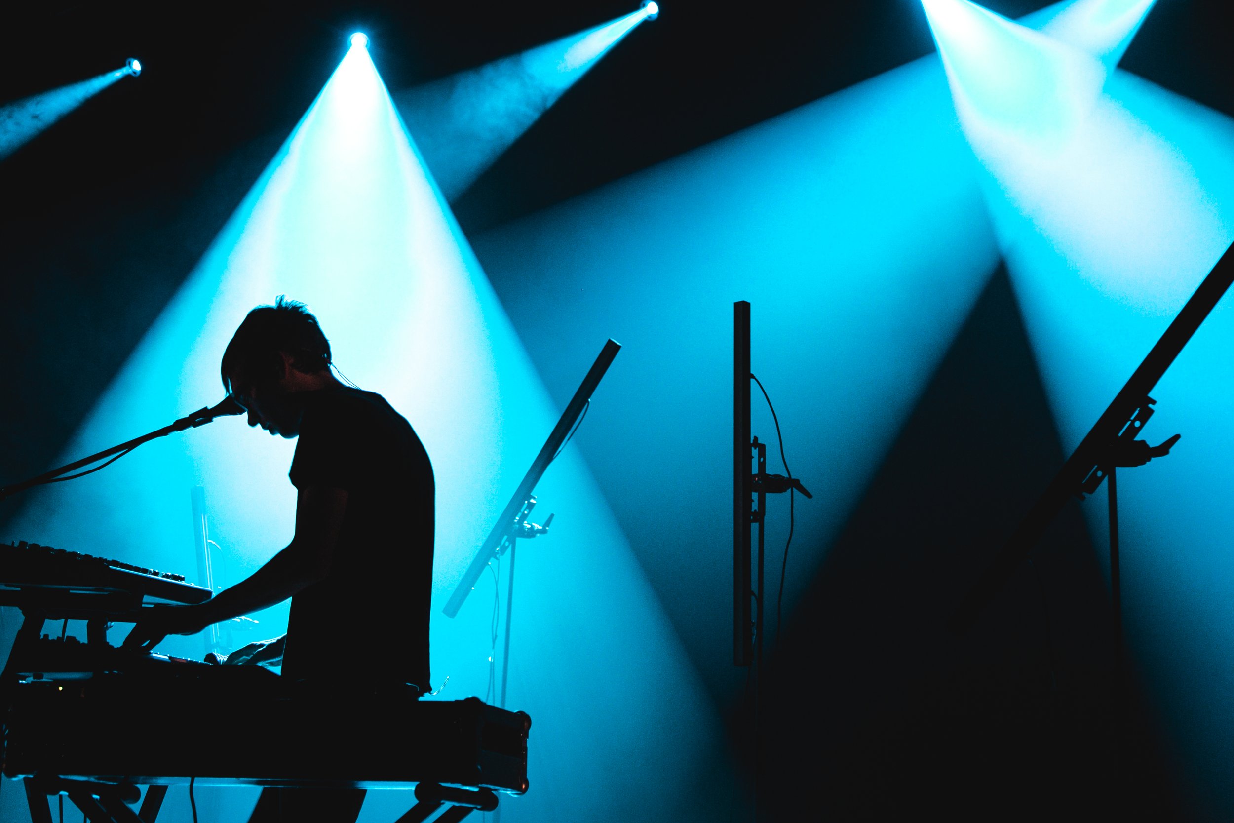 Silhouette d'un musicien jouant du clavier sur scène avec des éclairages bleus.