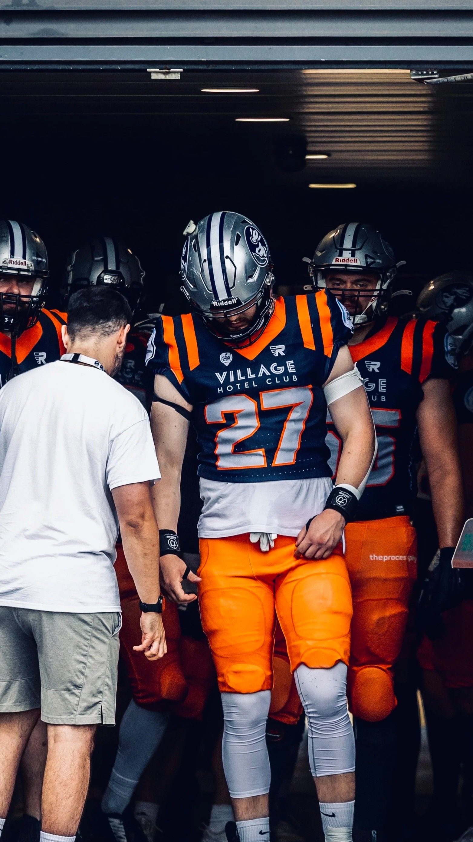 Football team members, wearing helmets and uniforms, preparing in a tunnel before a game.