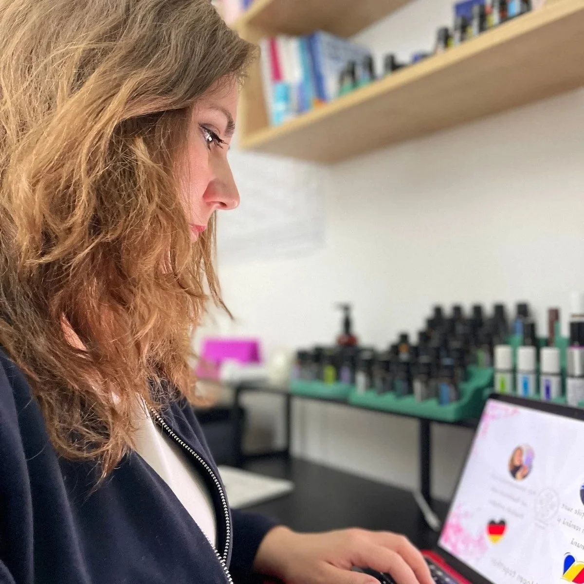 Elena, consultant wellness Blooming Health, studiind la laptop lângă colecția de uleiuri esențiale dōTERRA.